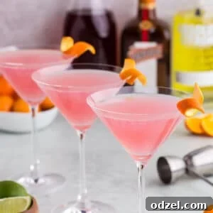 Three cosmopolitan martinis with alcohol bottles in the background.