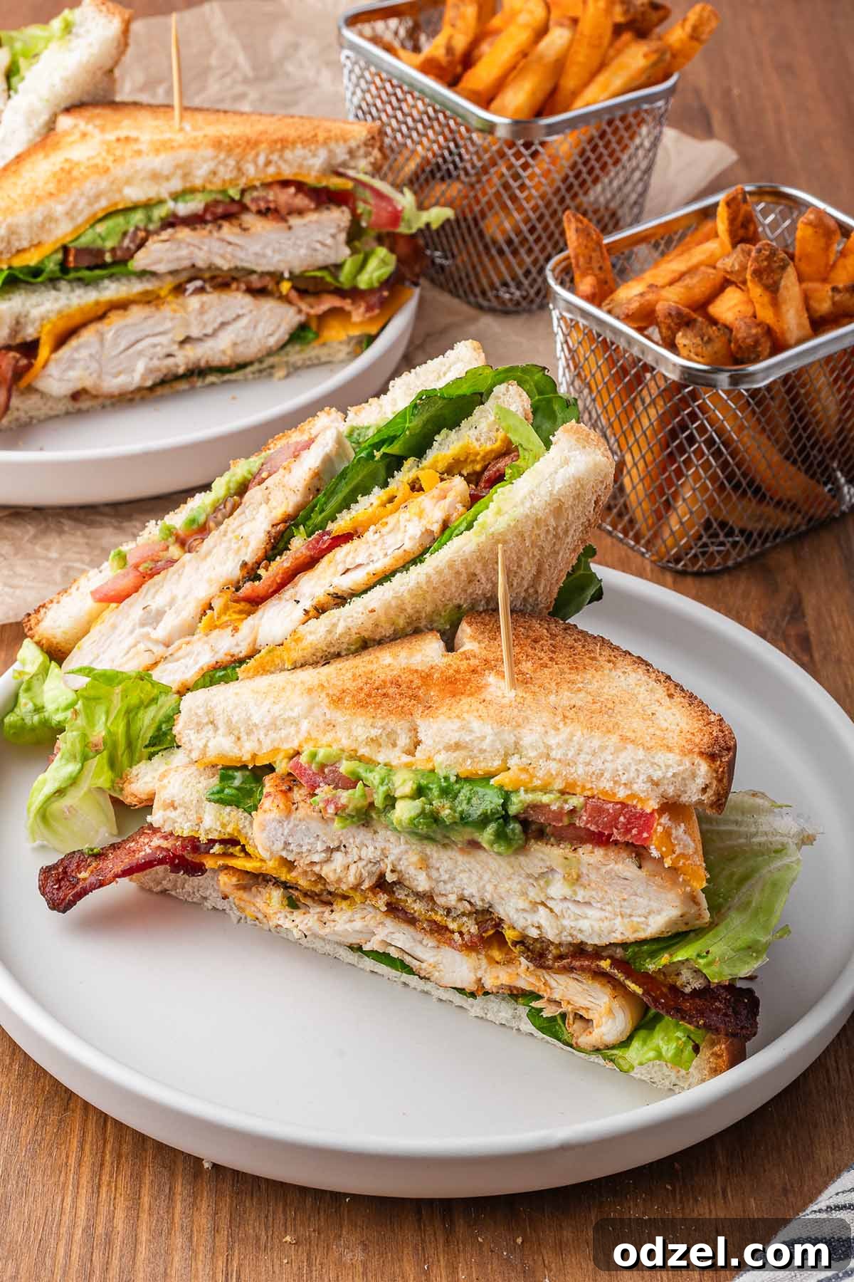 A perfectly assembled chicken club sandwich, cut in half and served with a side of golden French fries.