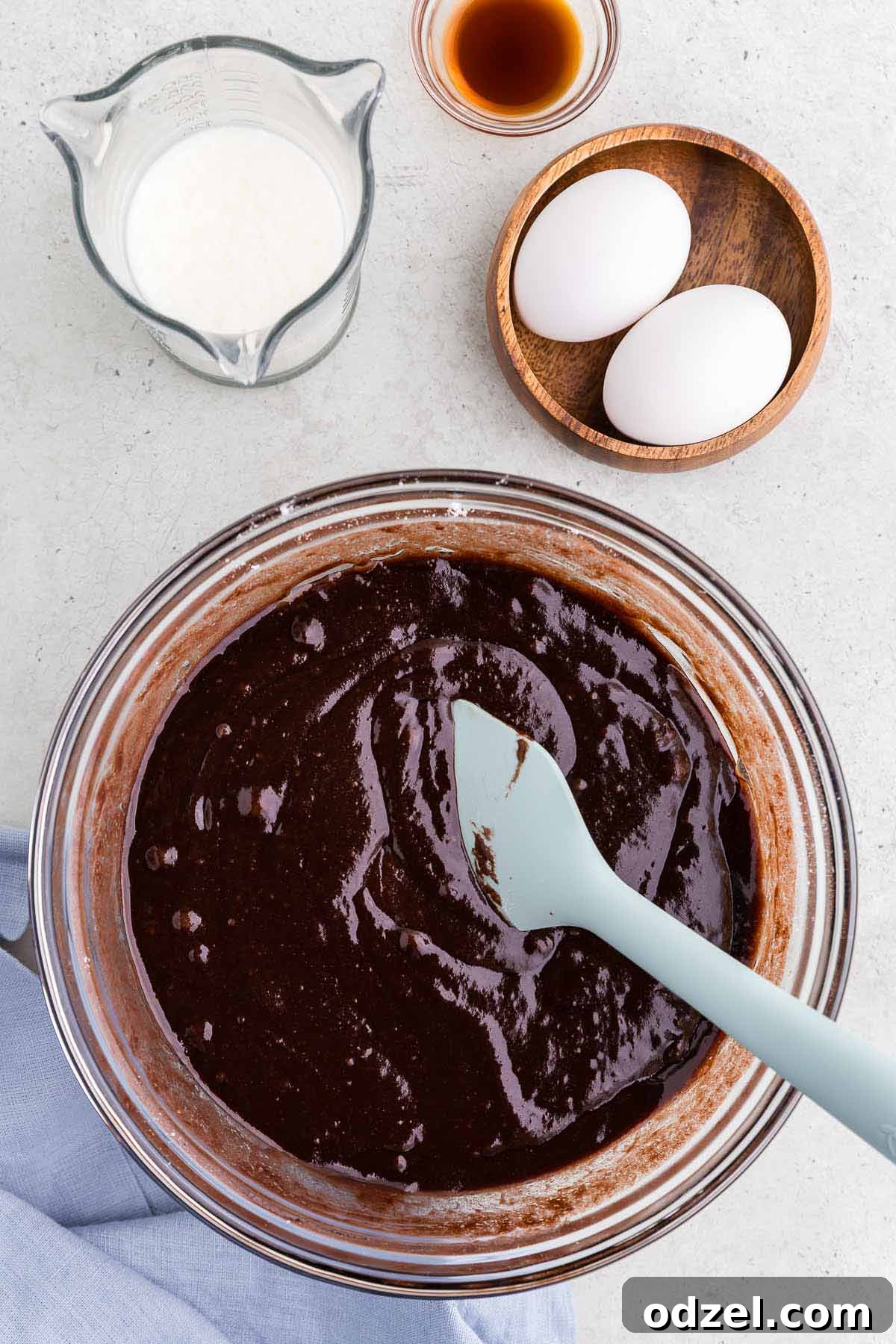 Chocolate cake batter in a large mixing bowl, with eggs, milk, and vanilla extract carefully placed beside it, ready for incorporation.
