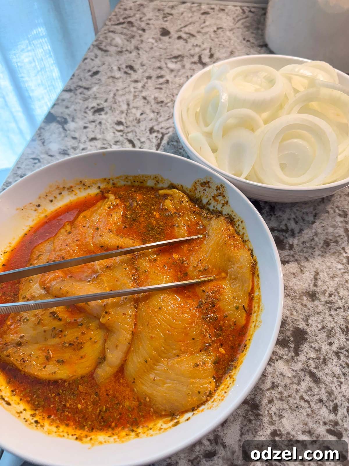 Raw chicken breasts soaking in a vibrant citrus and spice marinade, with thinly sliced raw onions prepared on the side.