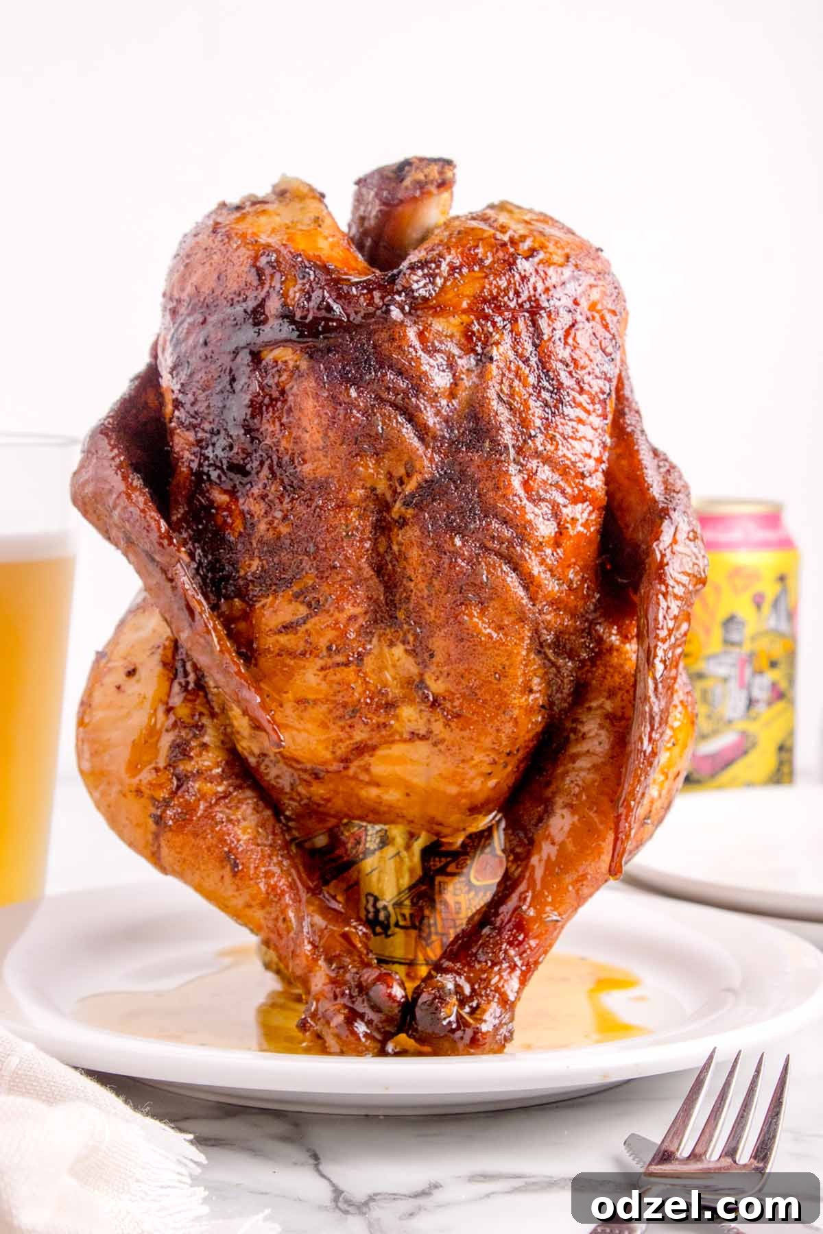 A beautifully golden and fully cooked whole chicken standing on a white plate, ready for carving.