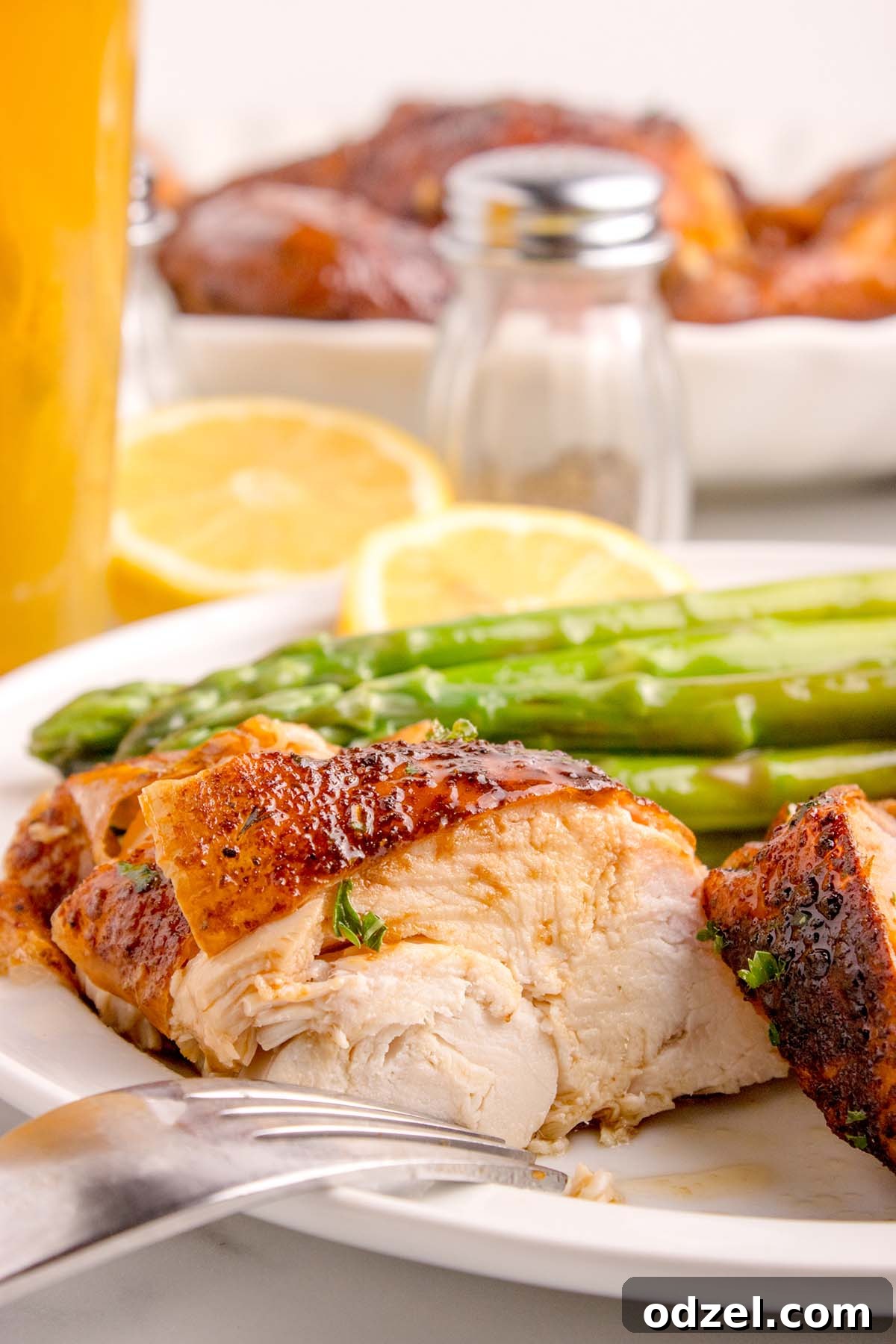 A serving of succulent chicken breast with fresh green asparagus spears on a white plate.