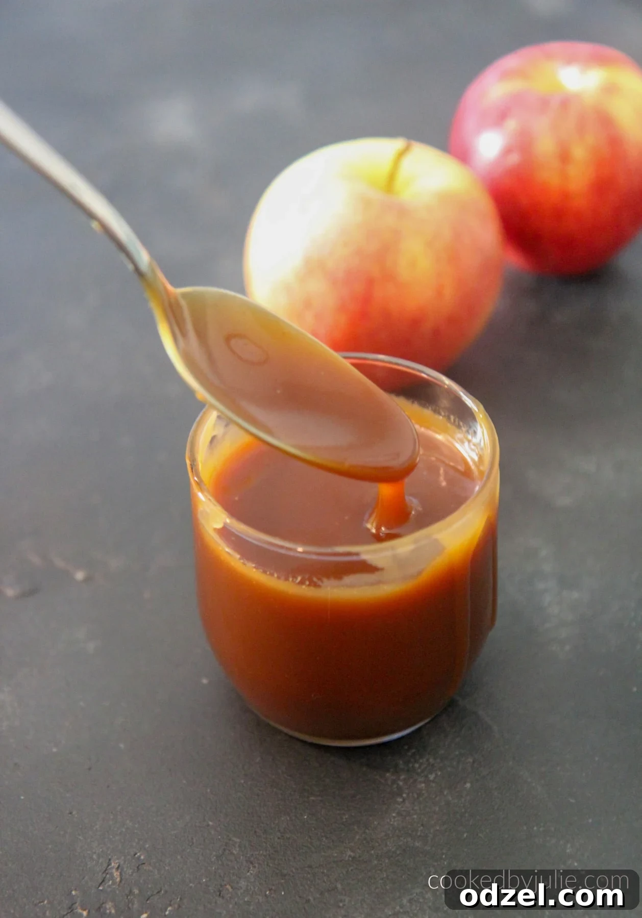 Velvety Smooth Caramel Sauce from Scratch 3 Close-up of golden, rich homemade caramel sauce drizzled from a spoon into a glass jar.