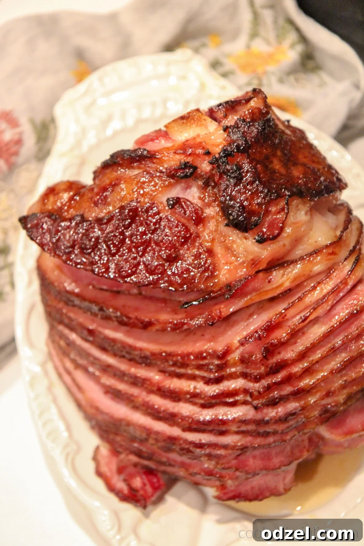 A whole, beautifully baked spiral ham with a glistening brown sugar glaze, presented on a pristine white serving platter, ready to be carved for a festive holiday meal.