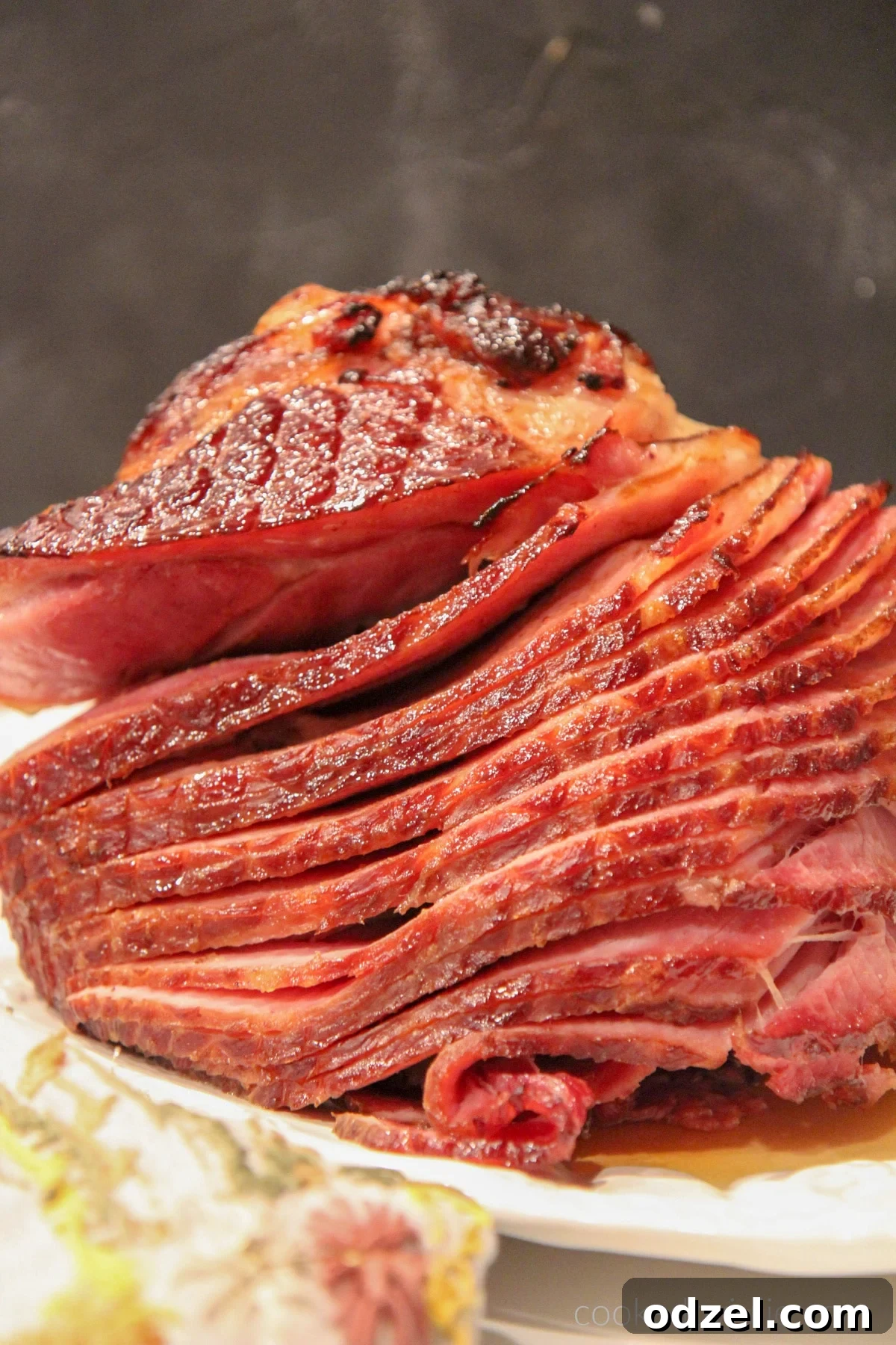 A delectable baked ham with a rich, glossy brown sugar glaze, presented on an elegant white platter against a sophisticated dark backdrop, ready to be served.