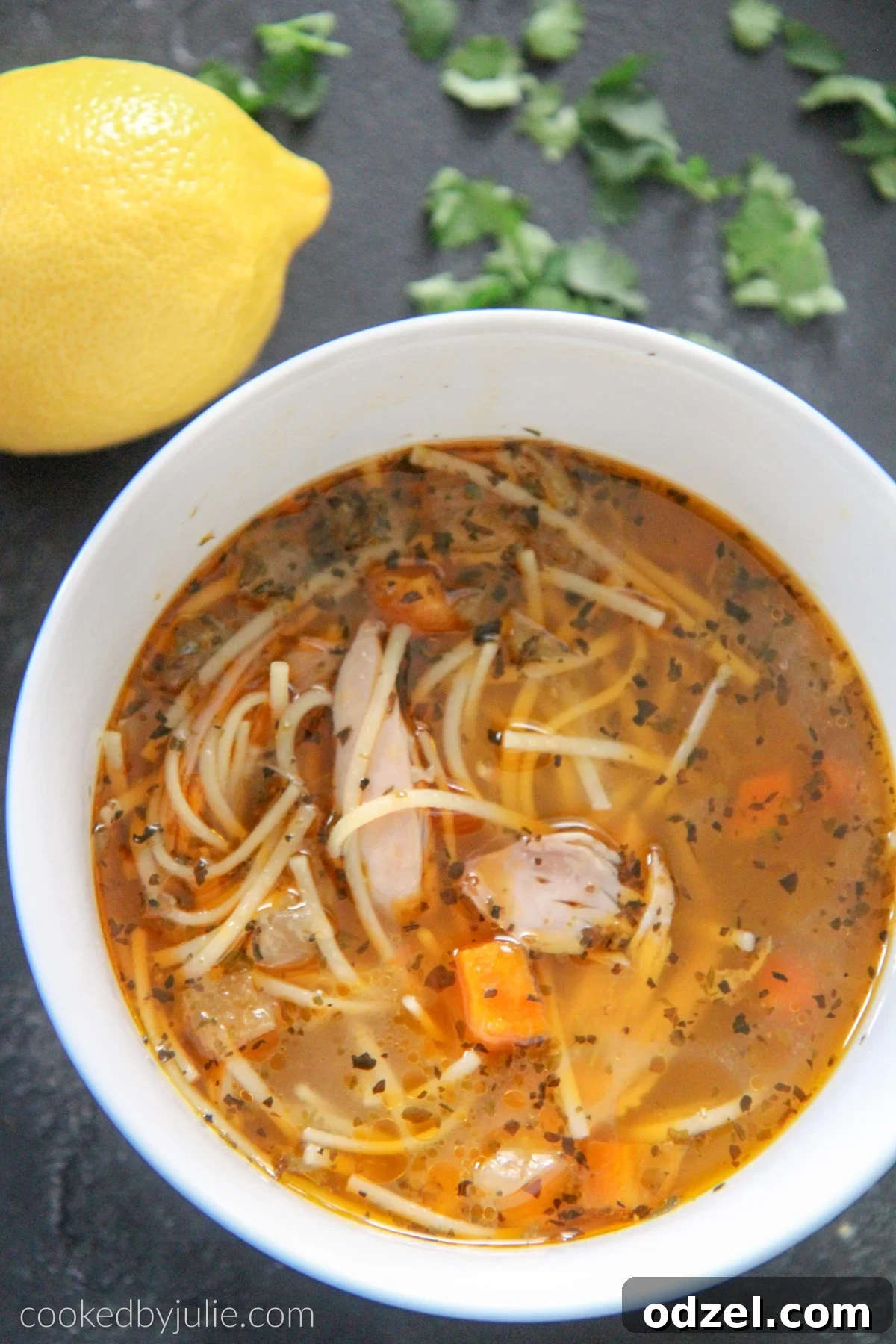 Flavorful chicken noodle soup served in a white bowl, garnished with fresh lemon wedges and parsley, ready to be enjoyed.