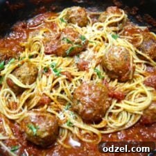A close-up of a serving of spicy spaghetti and meatballs with fresh basil garnish.