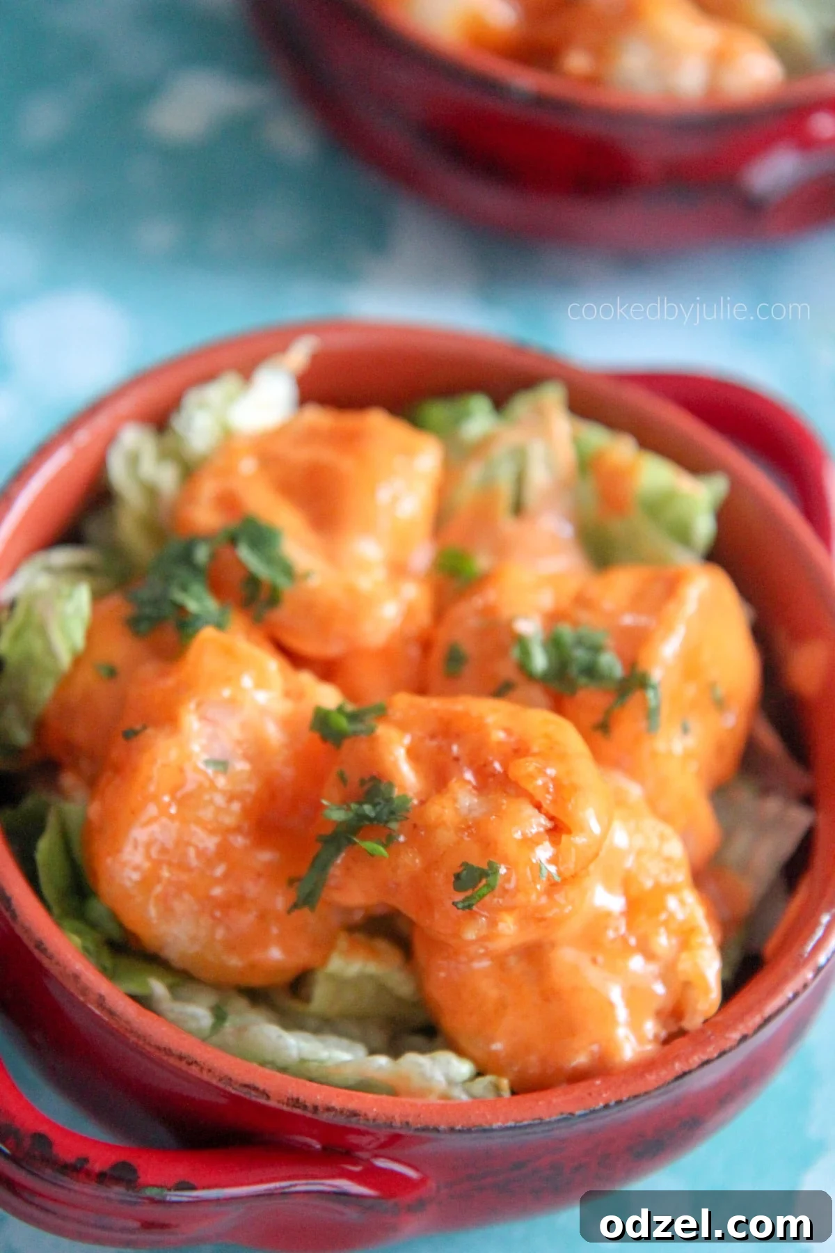 A vibrant red bowl filled with golden crispy Bang Bang Shrimp, garnished with fresh green lettuce beneath.