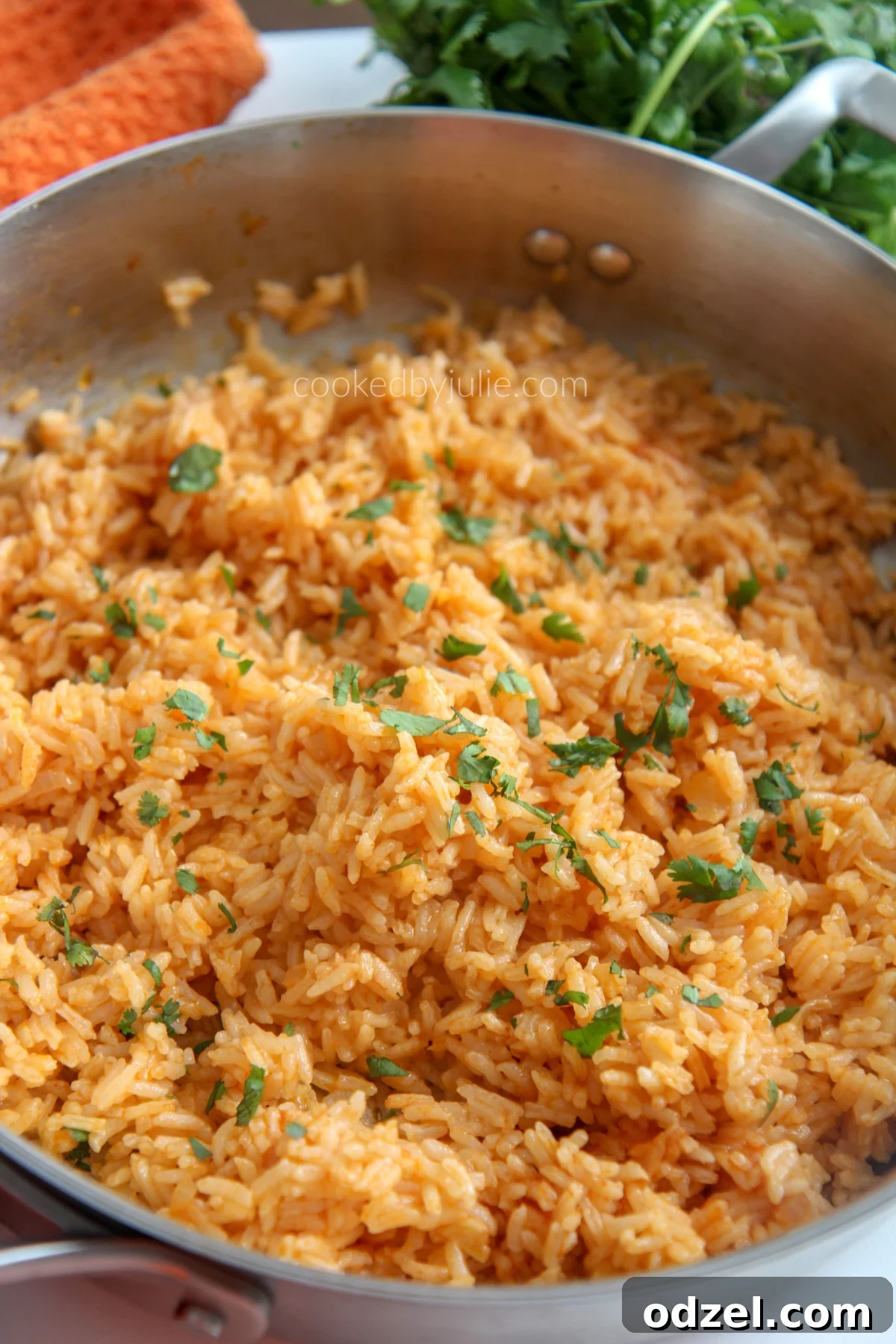 A skillet filled with Spanish rice with an orange kitchen towel and fresh cilantro in the background
