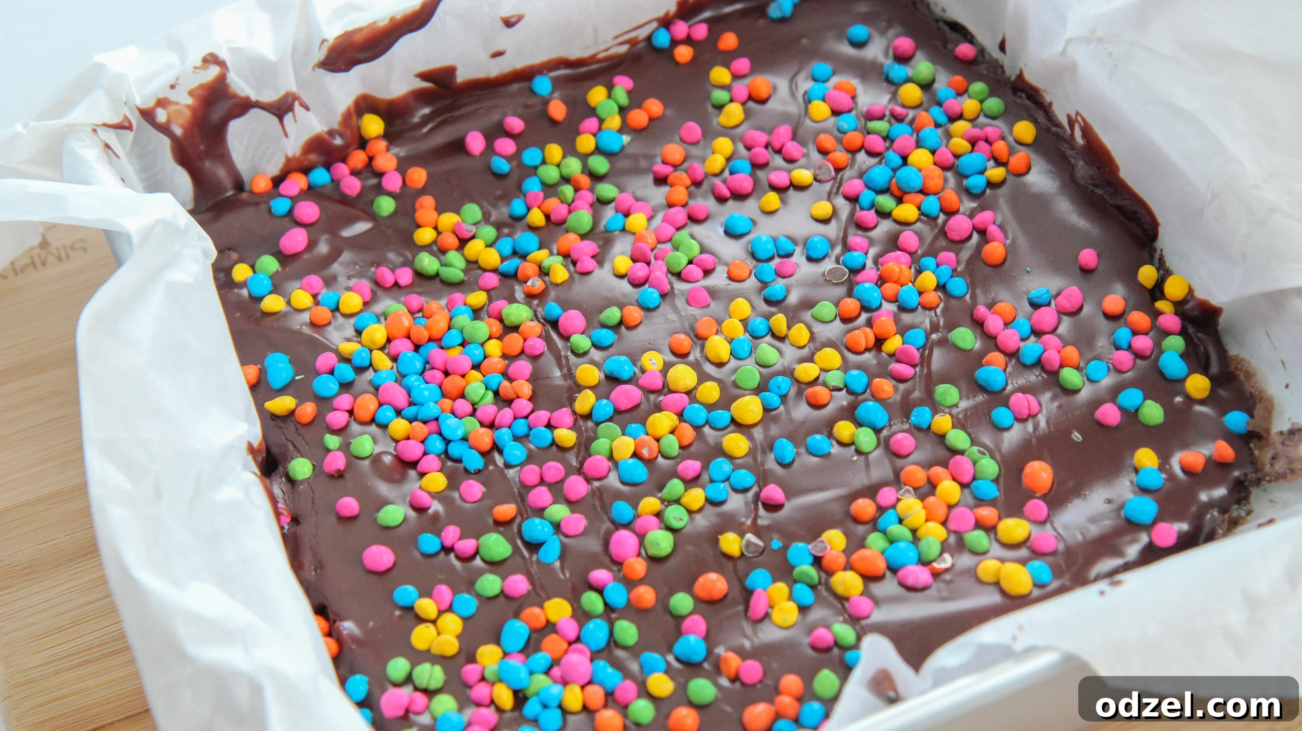 Dark Matter Brownies 3 A 9x9 inch baking dish filled with cooling cosmic brownies, lined with parchment paper, awaiting the chocolate ganache and colorful rainbow chips.