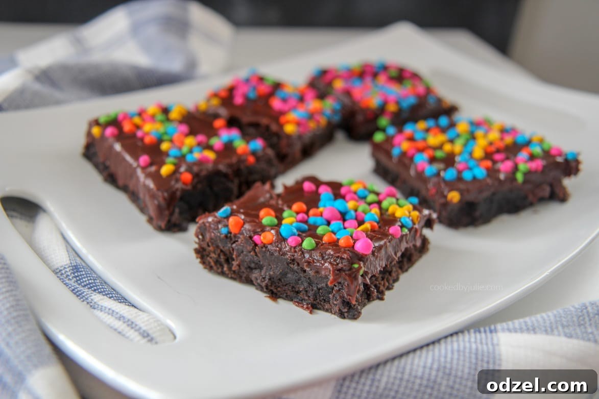 Dark Matter Brownies 4 Close-up of a stack of fudgy cosmic brownies on a white plate, with a blue and white striped kitchen towel draped beside them, highlighting their rich texture and colorful topping.