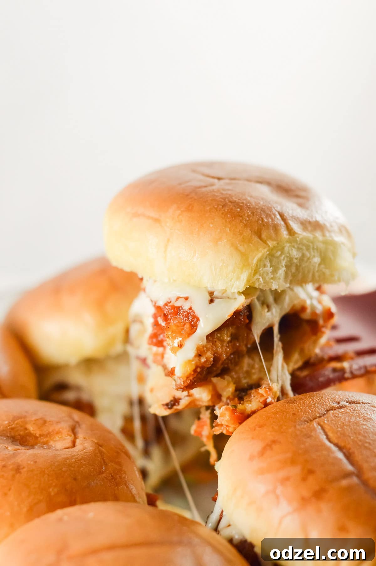 A spatula lifting a chicken parm slider from a the baking pan, showcasing the melted cheese and golden bun.
