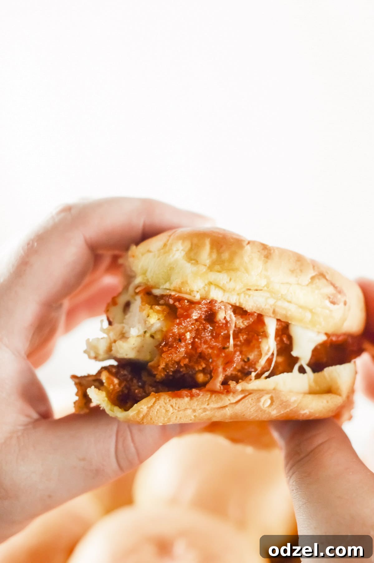 Two hands holding up a chicken parm slider, showcasing its size and delicious layers.
