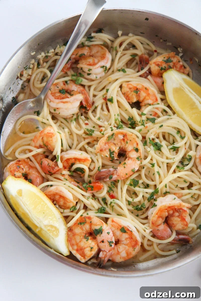 Close-up of shrimp scampi with spaghetti in a skillet, garnished with lemon wedges and a serving spoon.