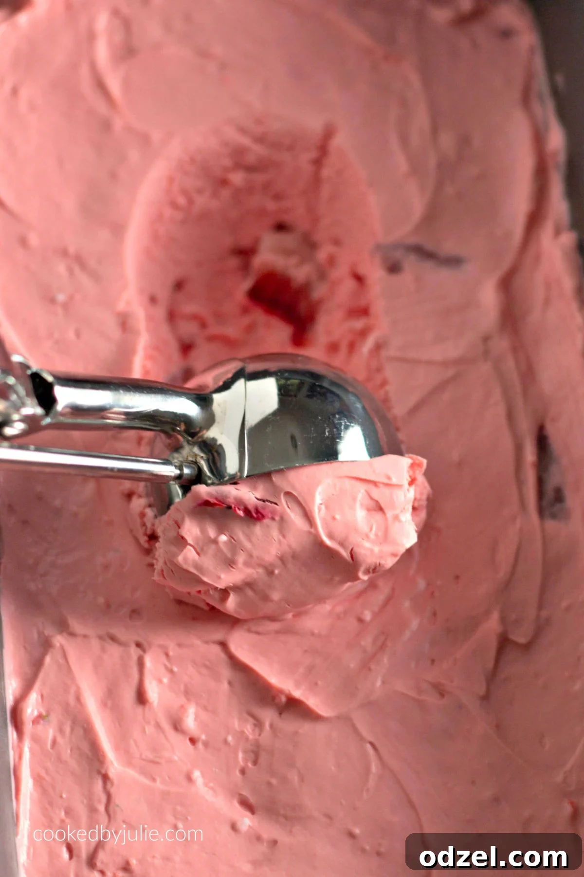 A bread pan filled with creamy strawberry fat bomb mixture, with an ice cream scoop poised to serve, showcasing its readiness for enjoyment.