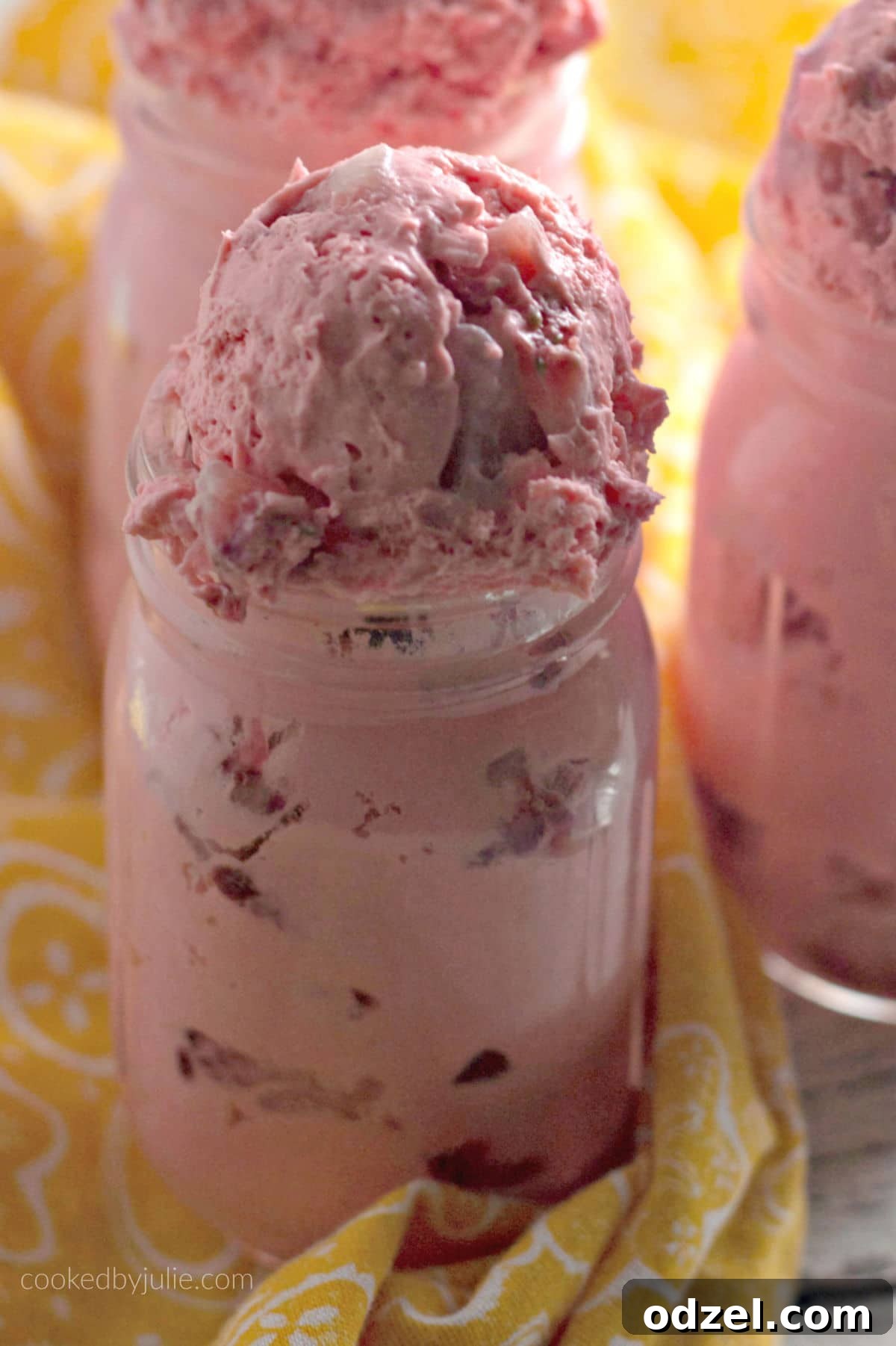 A close-up shot of three strawberry fat bombs served in small mason jars, beautifully garnished, with a yellow towel nearby, emphasizing their appetizing appeal.
