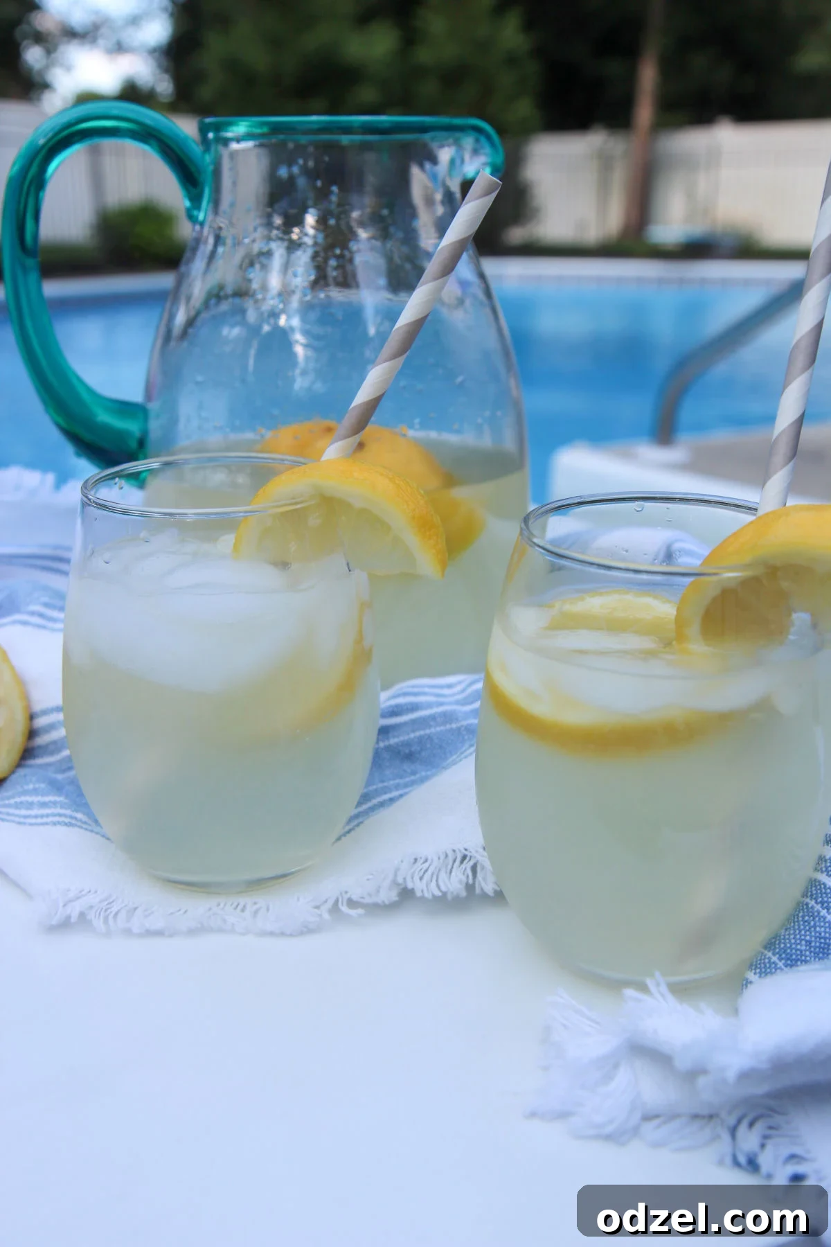 two glasses of lemonade and a glass pitcher in the background