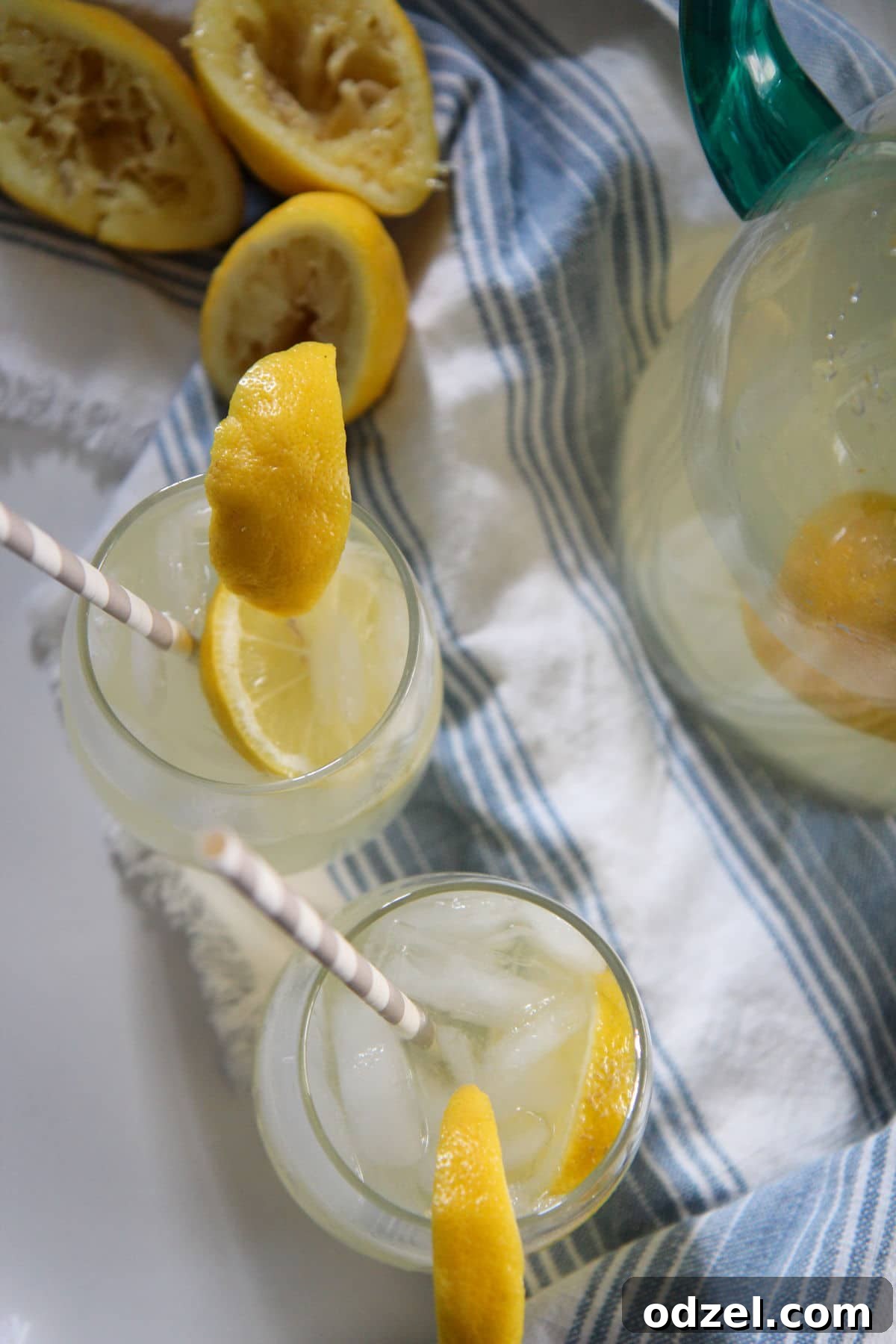 2 glasses of lemonade with straws on a white table with a blue table cloth