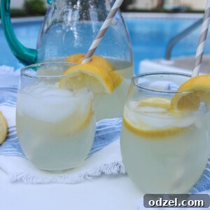 two glasses of lemonade and a glass pitcher in the background