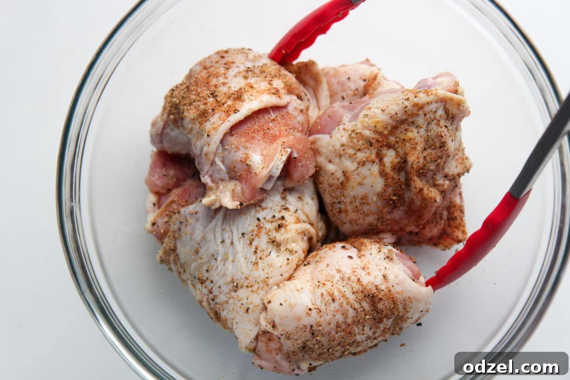 Chicken thighs seasoned with spices in a glass bowl, ready for cooking