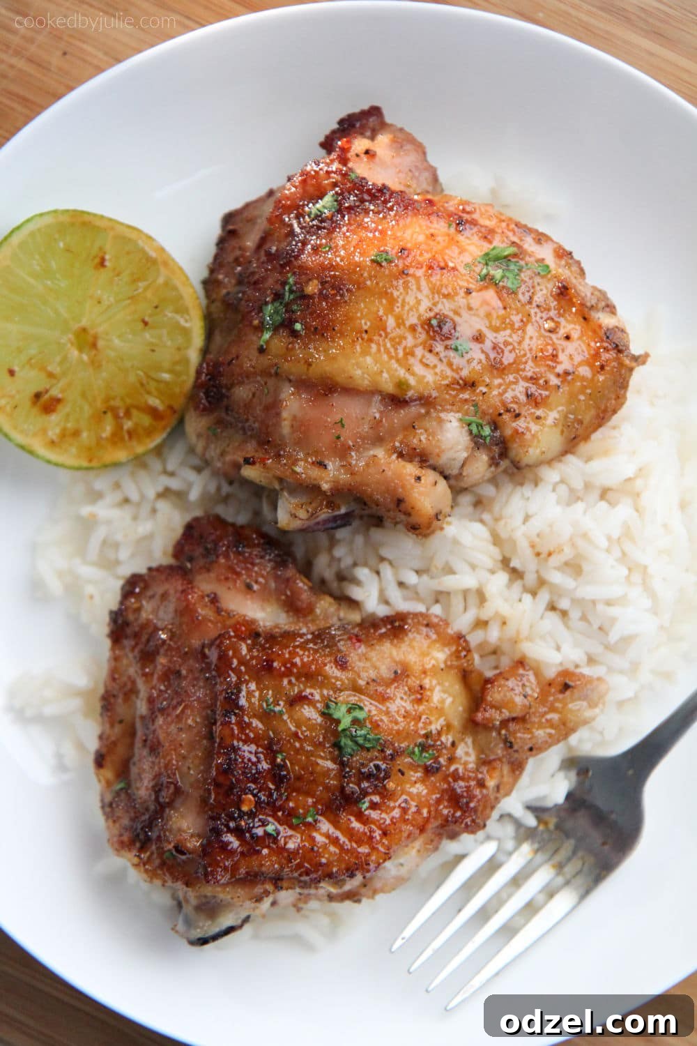 Two honey lime chicken thighs served over rice with a lime wedge and fresh cilantro on a white plate