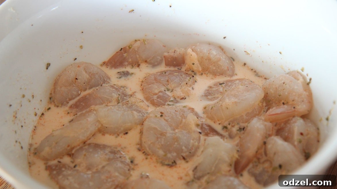 Raw shrimp, an assortment of spices, and whole milk are presented in a white bowl, ready for the initial marinade.