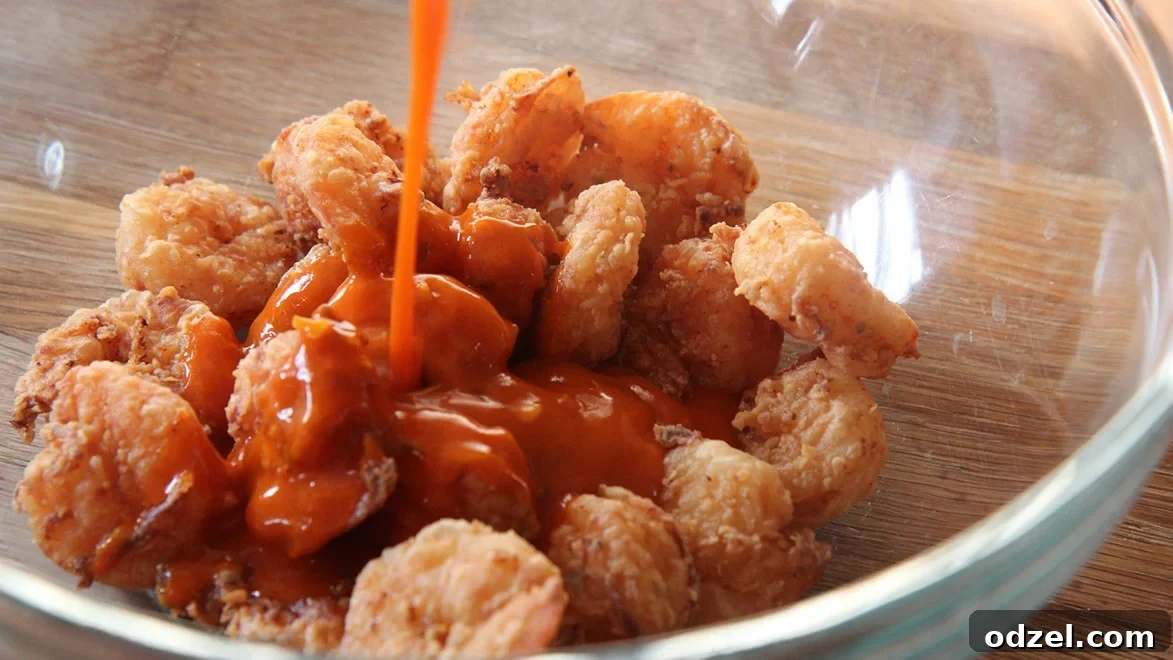 Perfectly fried shrimp are shown in a bowl, with a rich buffalo sauce being generously poured over them, ready for tossing.