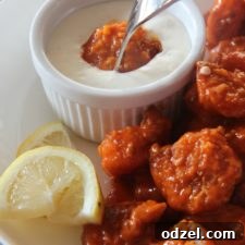 Close-up of crispy, golden-brown buffalo shrimp coated in spicy sauce, garnished with fresh herbs, in a bowl.