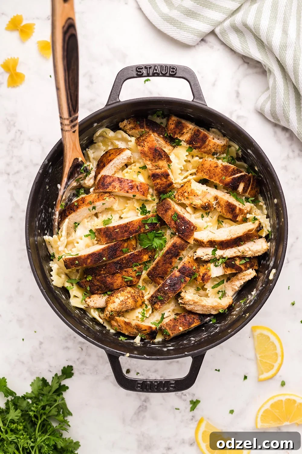 Cajun chicken, farfalle pasta, parsley, and a wooden spoon in a black skillet.