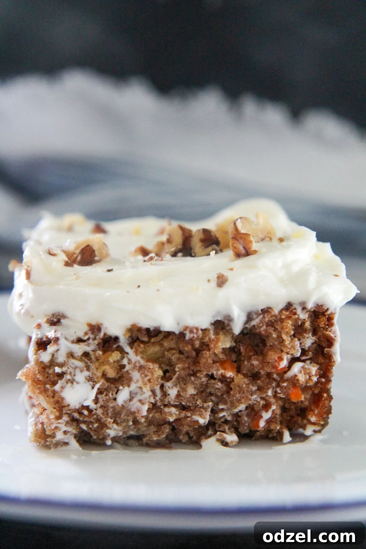 A close-up, mouth-watering view of a slice of carrot cake, showcasing its moist texture, visible shredded carrots, and a generous layer of creamy white frosting.