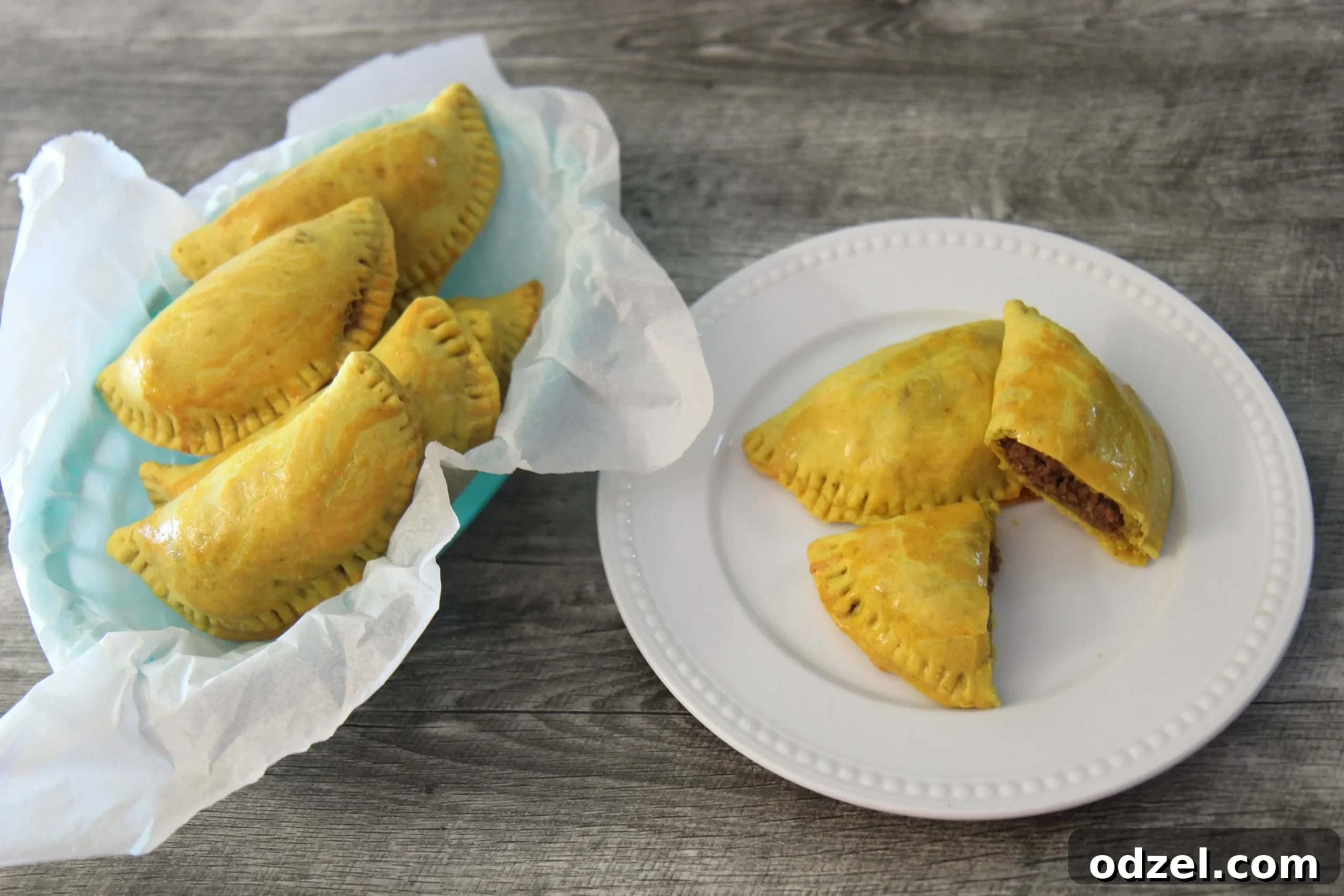 A rustic blue basket filled with five golden Jamaican Beef Patties, alongside two on a white plate, showcasing their inviting appeal.