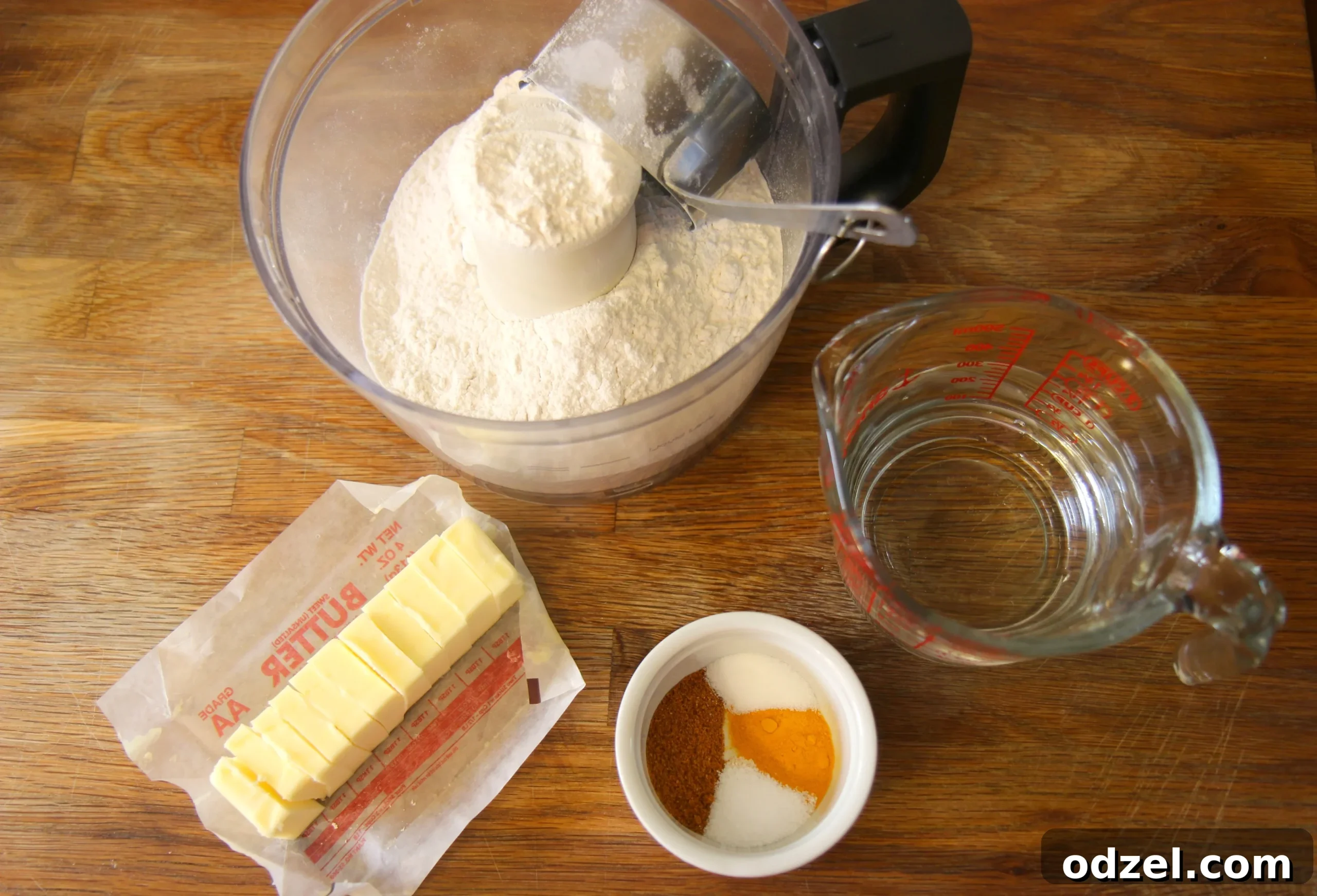 A food processor bowl filled with flour, butter pieces, and spices, ready for mixing to form the dough.