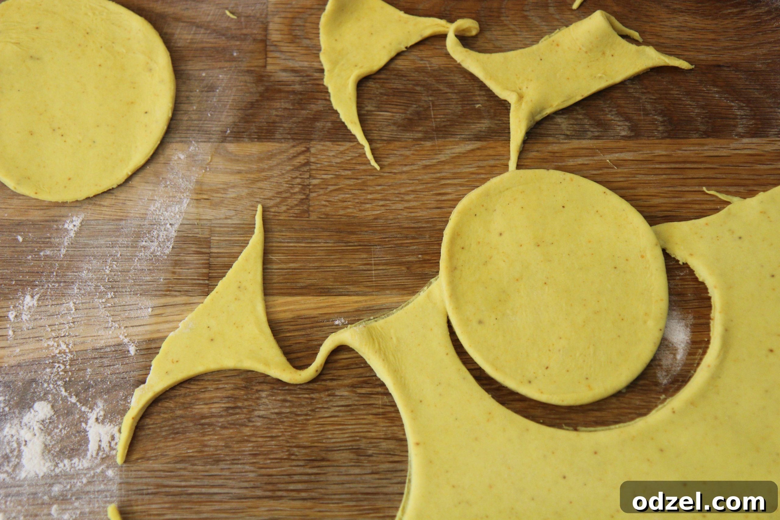 Circular cutouts of yellow dough neatly arranged on a floured surface, ready for filling.