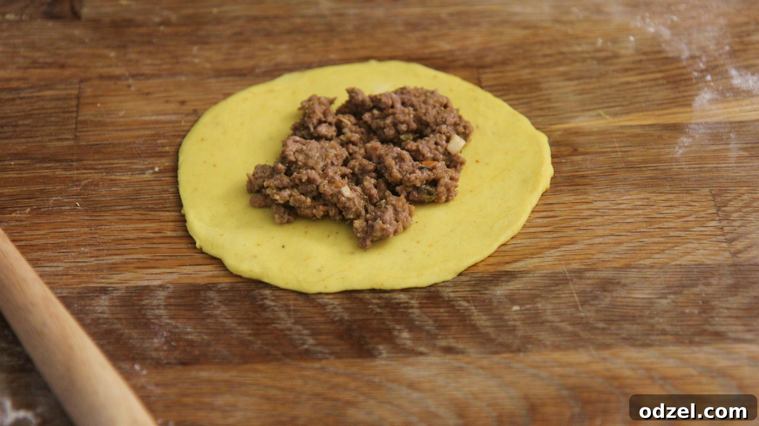 A single disc of golden dough filled with a generous scoop of seasoned ground beef mixture, ready to be folded.