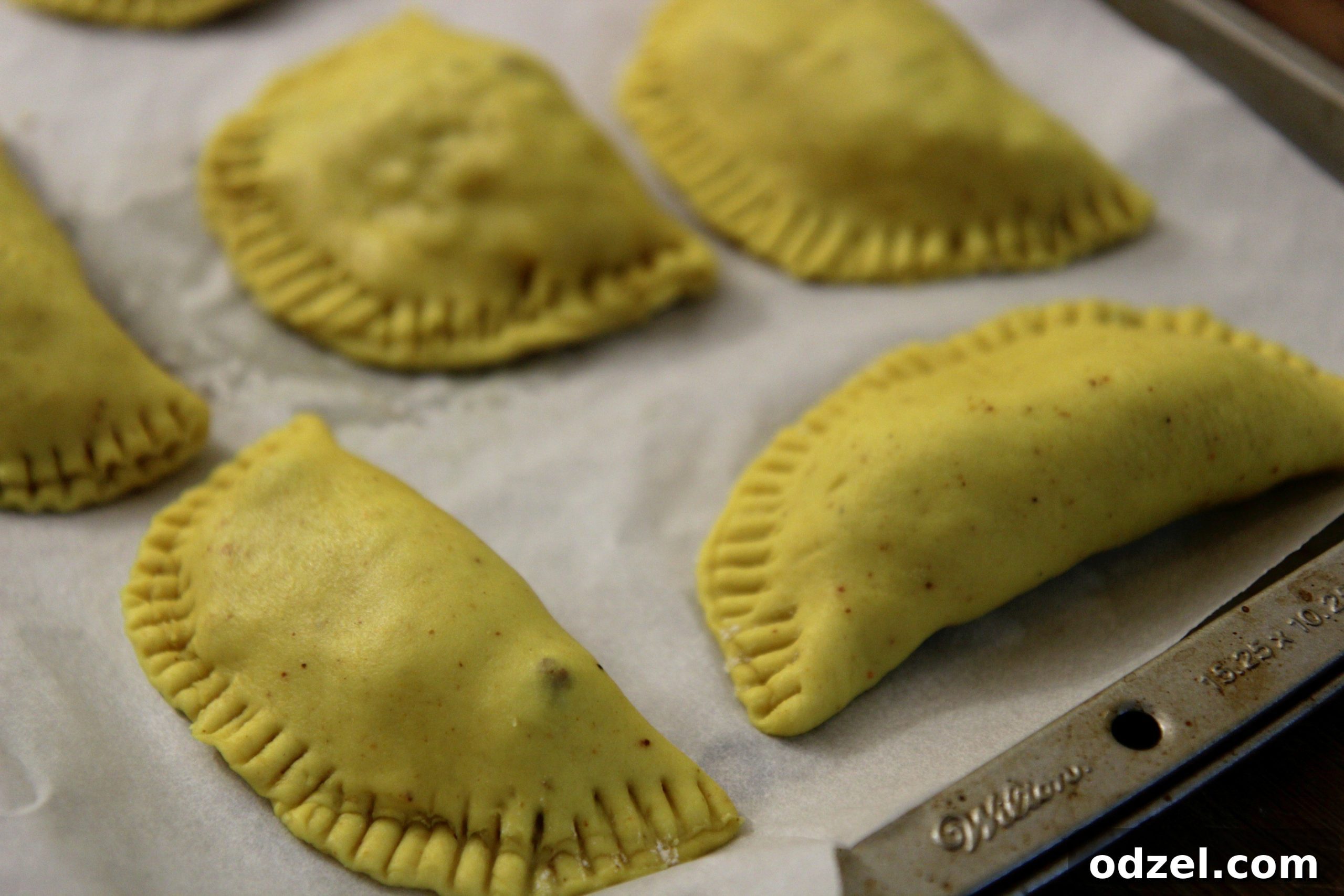 Several unbaked Jamaican Beef Patties neatly arranged on a baking sheet, brushed with egg wash and ready for the oven.
