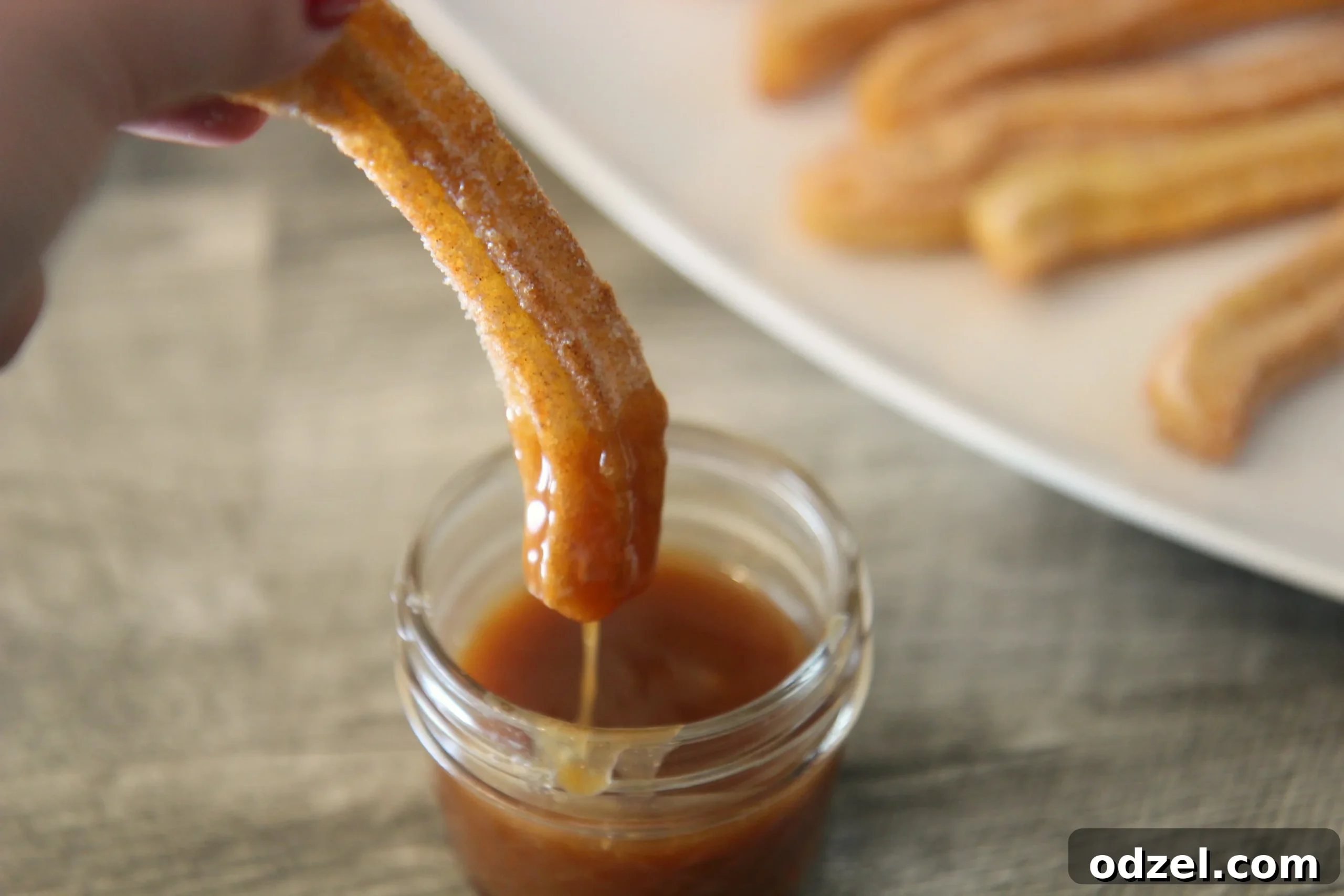 A churro is dipped into a bowl of golden homemade caramel sauce, showcasing its delicious pairing.