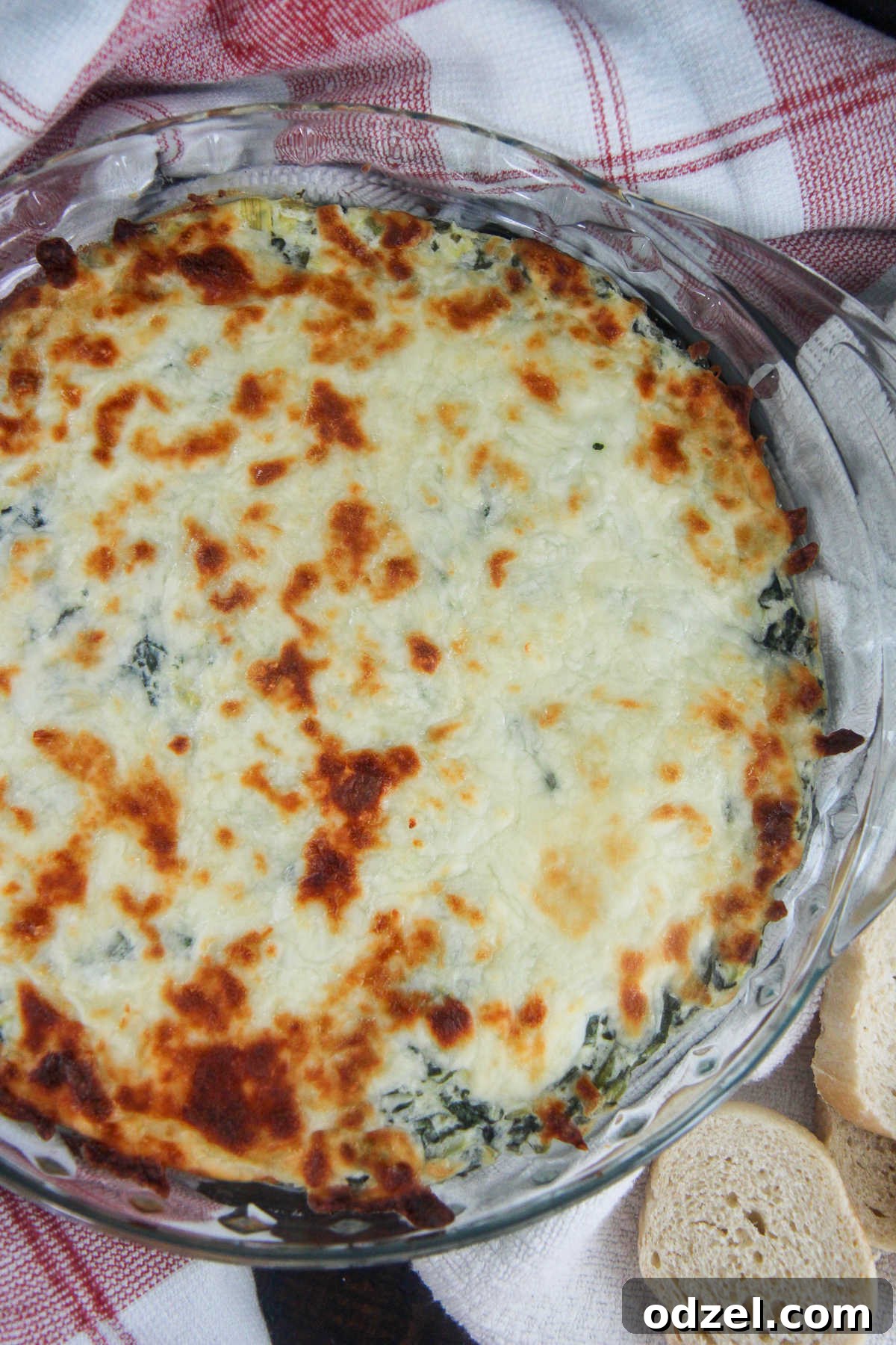 spinach artichoke dip in a glass bowl with bread on the side