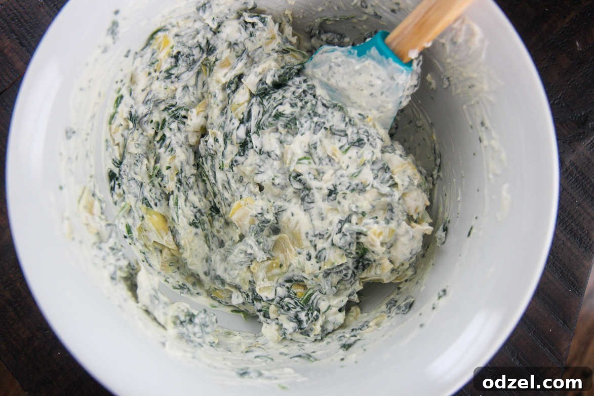 spinach artichoke dip mixture in a white bowl with a blue spatula