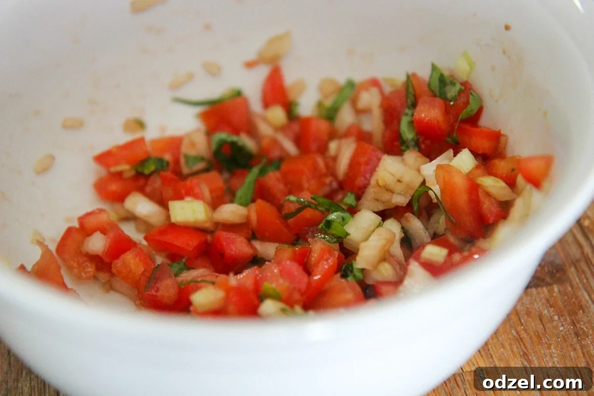 Tuscan Chicken Bruschetta 3 A small white bowl filled with freshly diced Roma tomatoes, finely chopped red onions, and elegantly sliced green basil ribbons, ready to be mixed for a vibrant bruschetta topping.