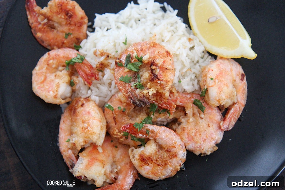 Hawaiian Garlic Shrimp Feast 3 shrimp and rice on a dark plate with a lemon wedge