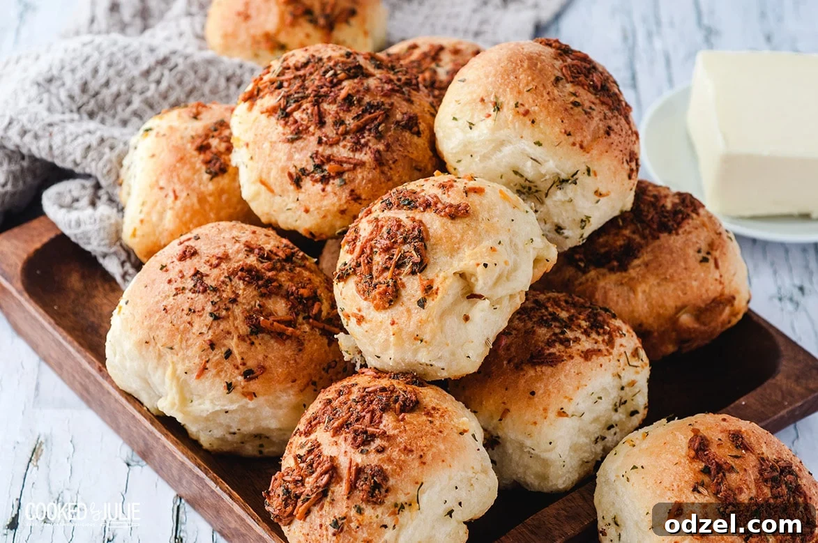 Ultimate Garlic Parmesan Dinner Rolls 4 Freshly baked golden brown garlic parmesan dinner rolls on a wooden board with a small bowl of melted butter