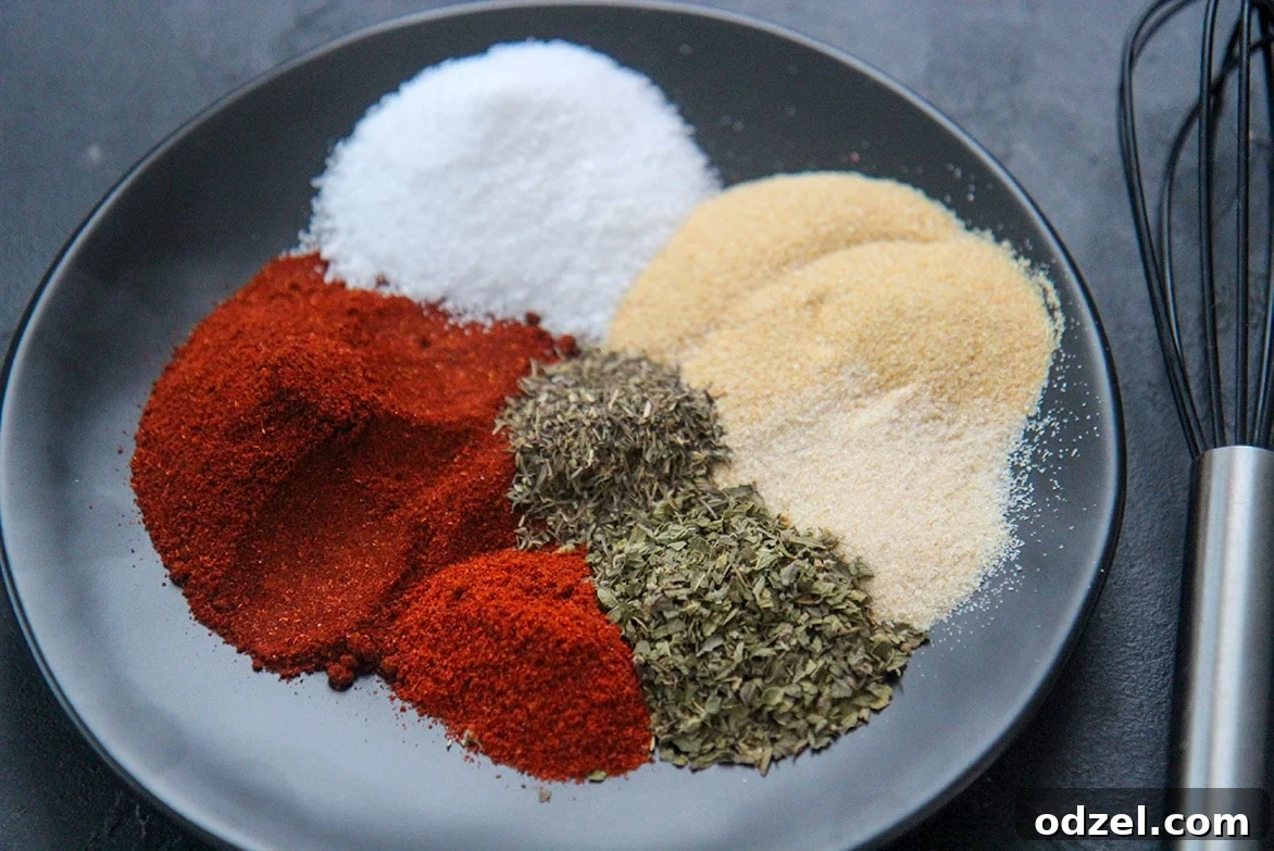 Louisiana's Fiery Spice Blend 3 Seven essential spices for Cajun seasoning laid out on a dark plate with a whisk beside them