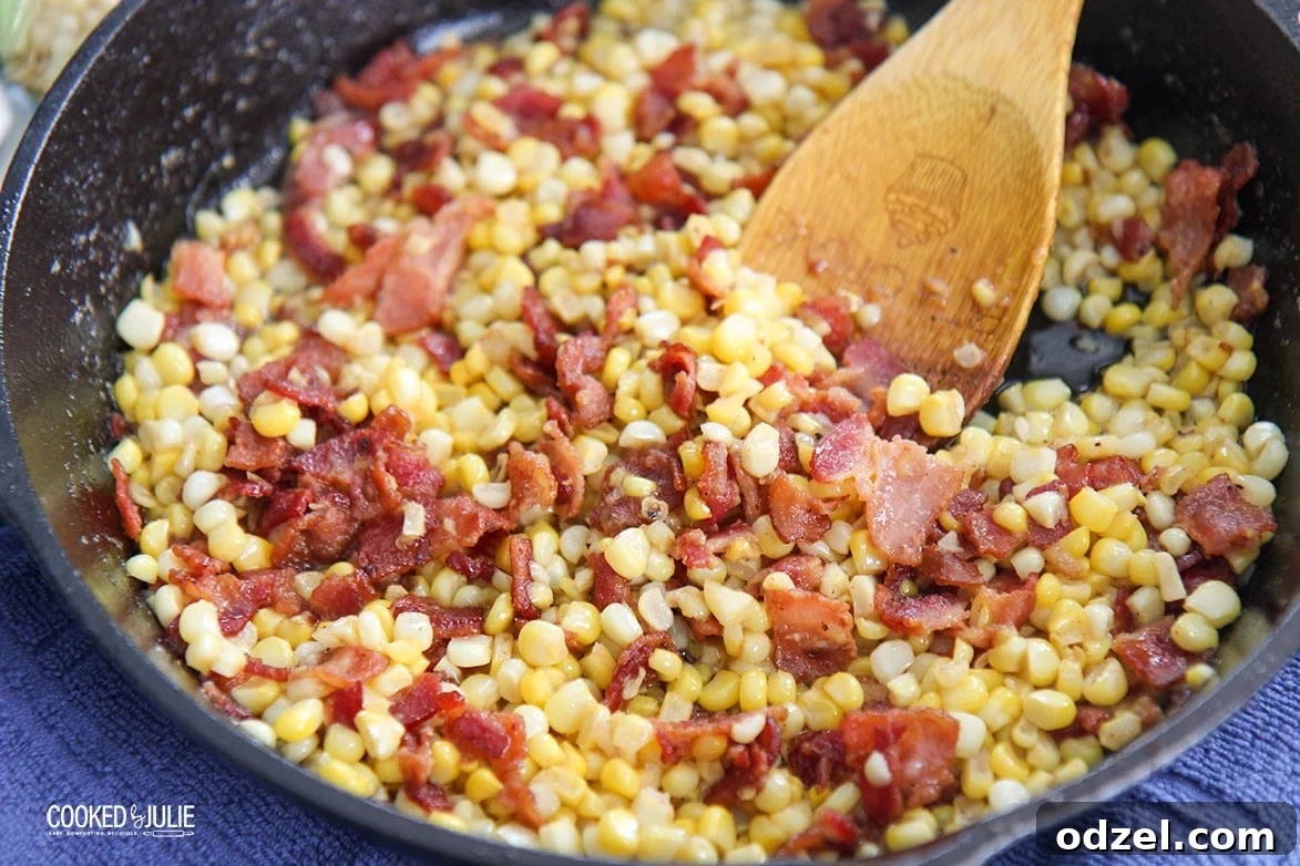 Bacon-Kissed Southern Fried Corn 3 Overhead shot of Southern fried corn with bacon and a wooden spoon in a cast iron skillet, ready to be served.