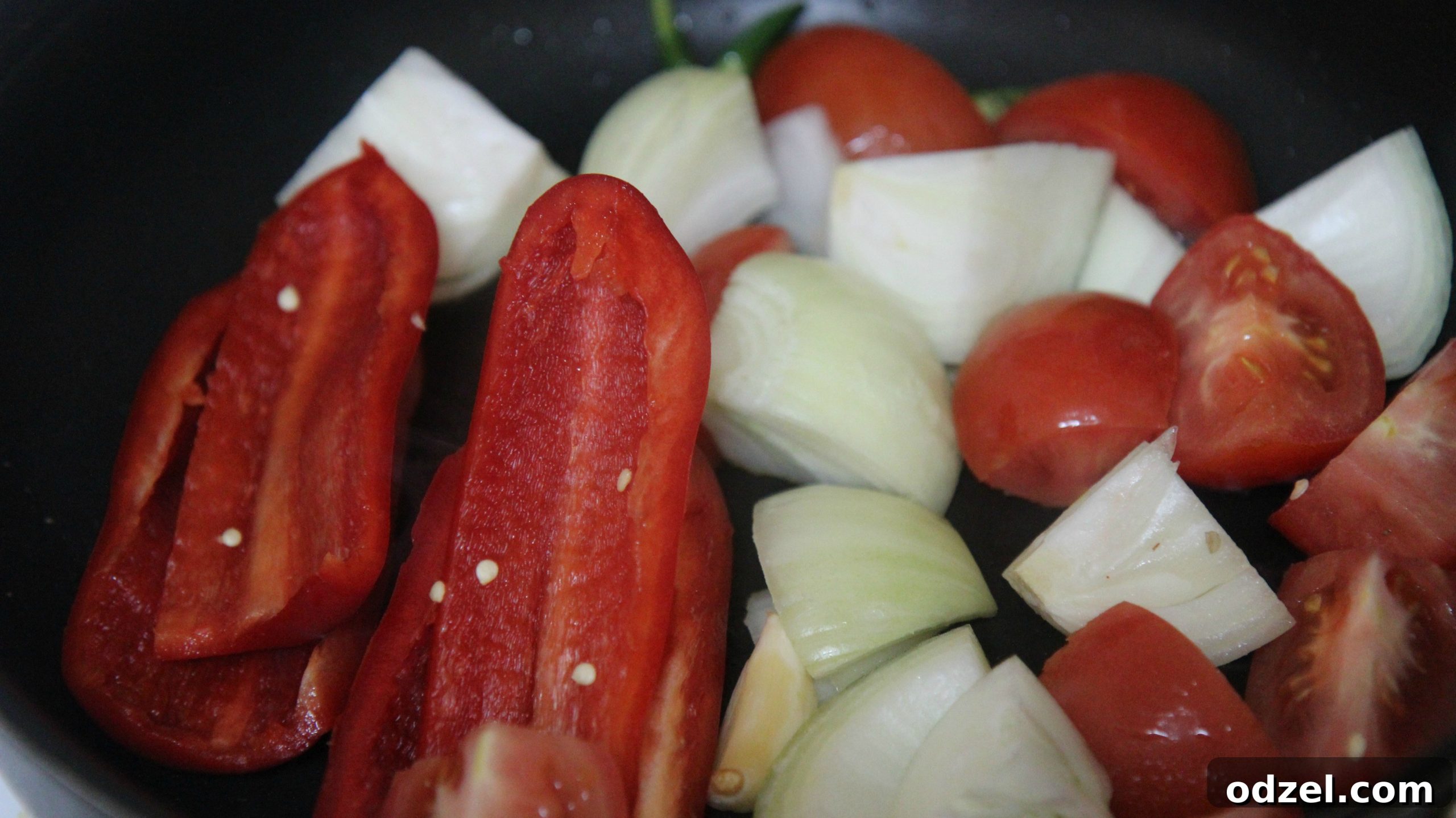 Sautéing fresh onions, tomatoes, and bell peppers in a black skillet for the soup base.