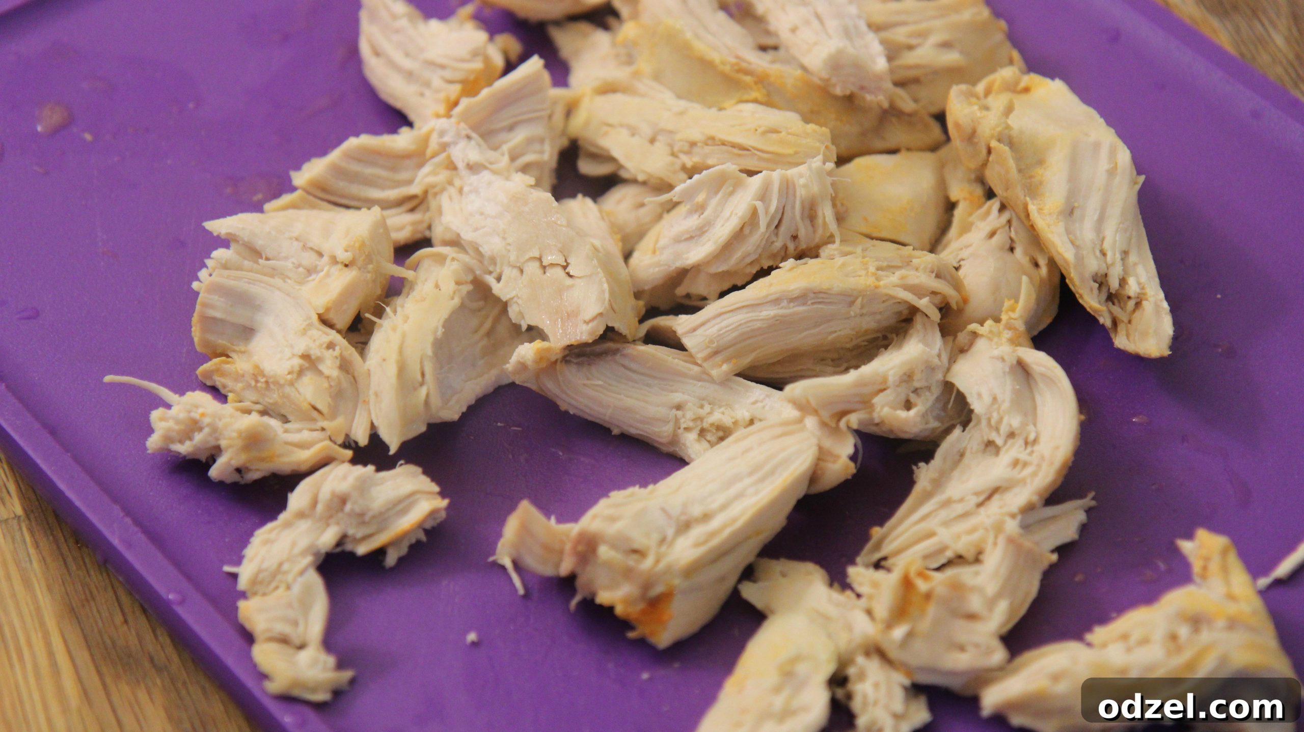 Perfectly shredded chicken breast on a purple cutting board, prepared for adding to the soup.