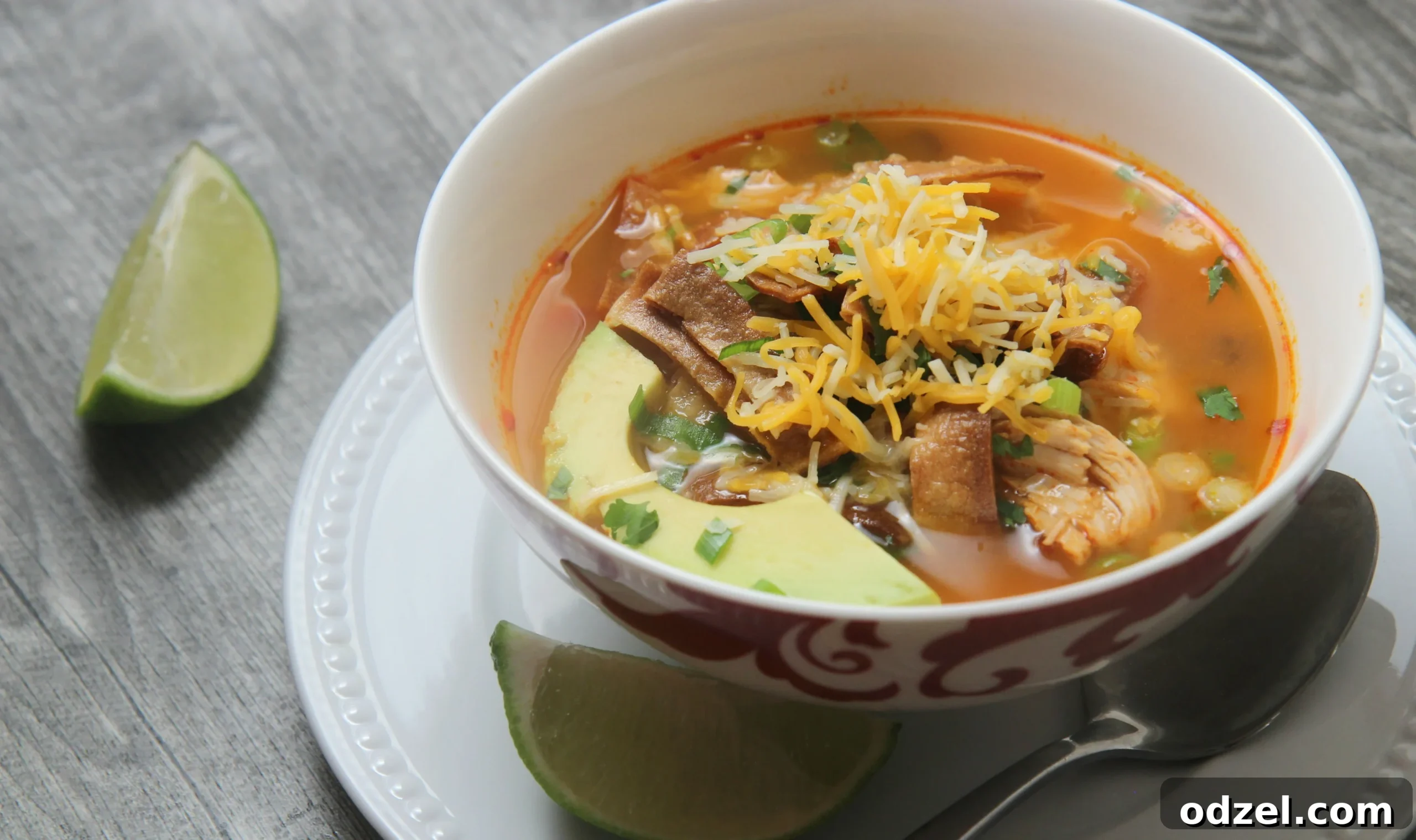 Close-up of a serving of spicy chicken tortilla soup, richly garnished with avocado, cheddar cheese, and crispy tortilla strips.