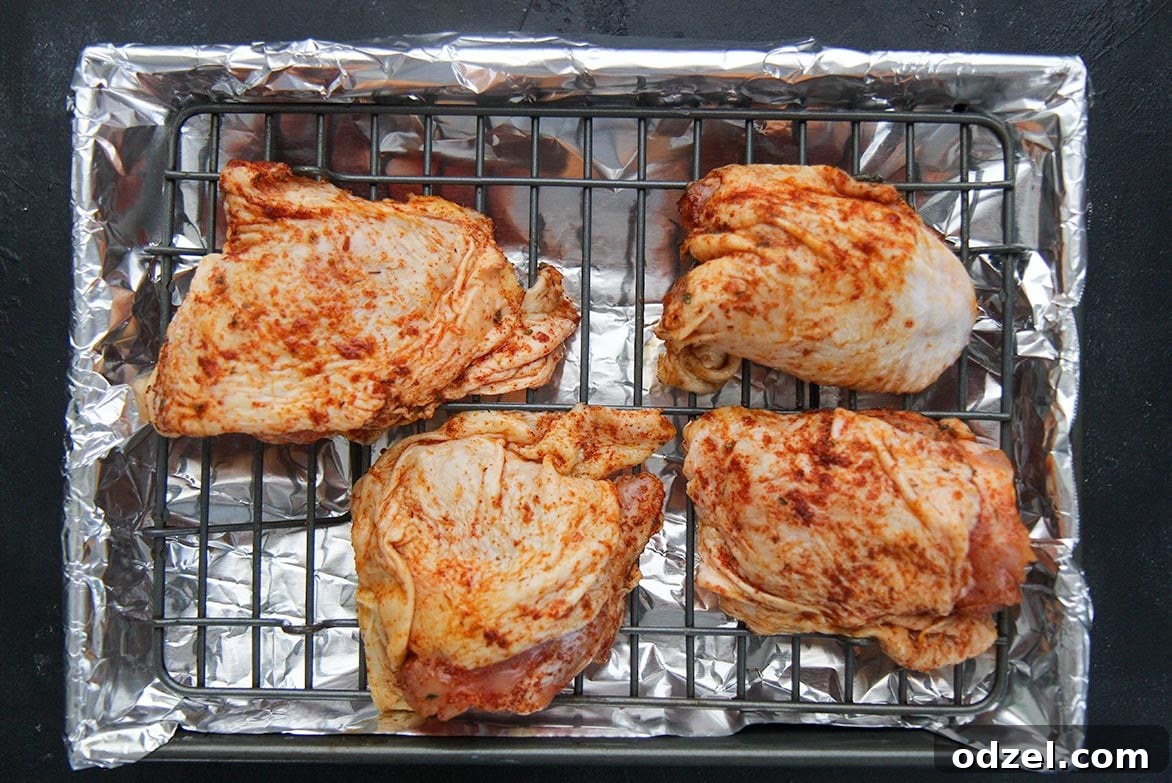 Four pieces of raw seasoned chicken thighs on a baking sheet, ready for the oven