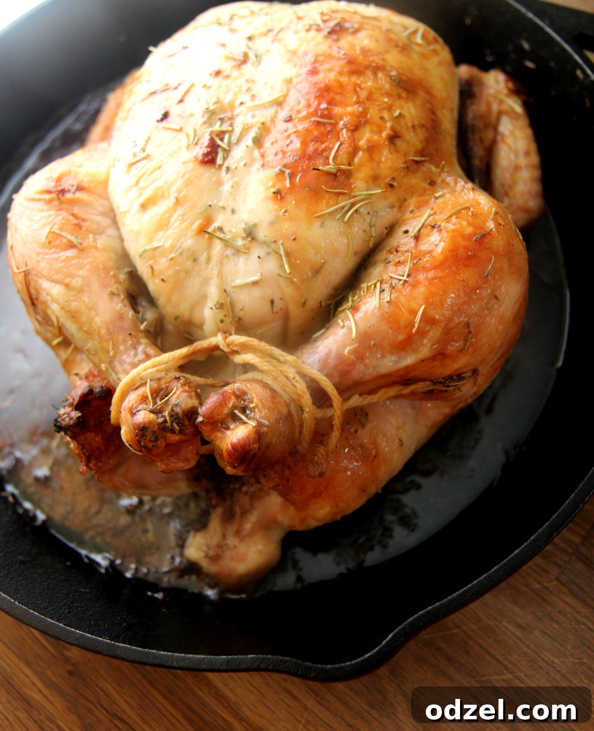 A beautifully roasted whole chicken, golden brown with crispy skin, garnished with fresh herbs, smothered in herb butter and roasted to perfection, ready to be carved.