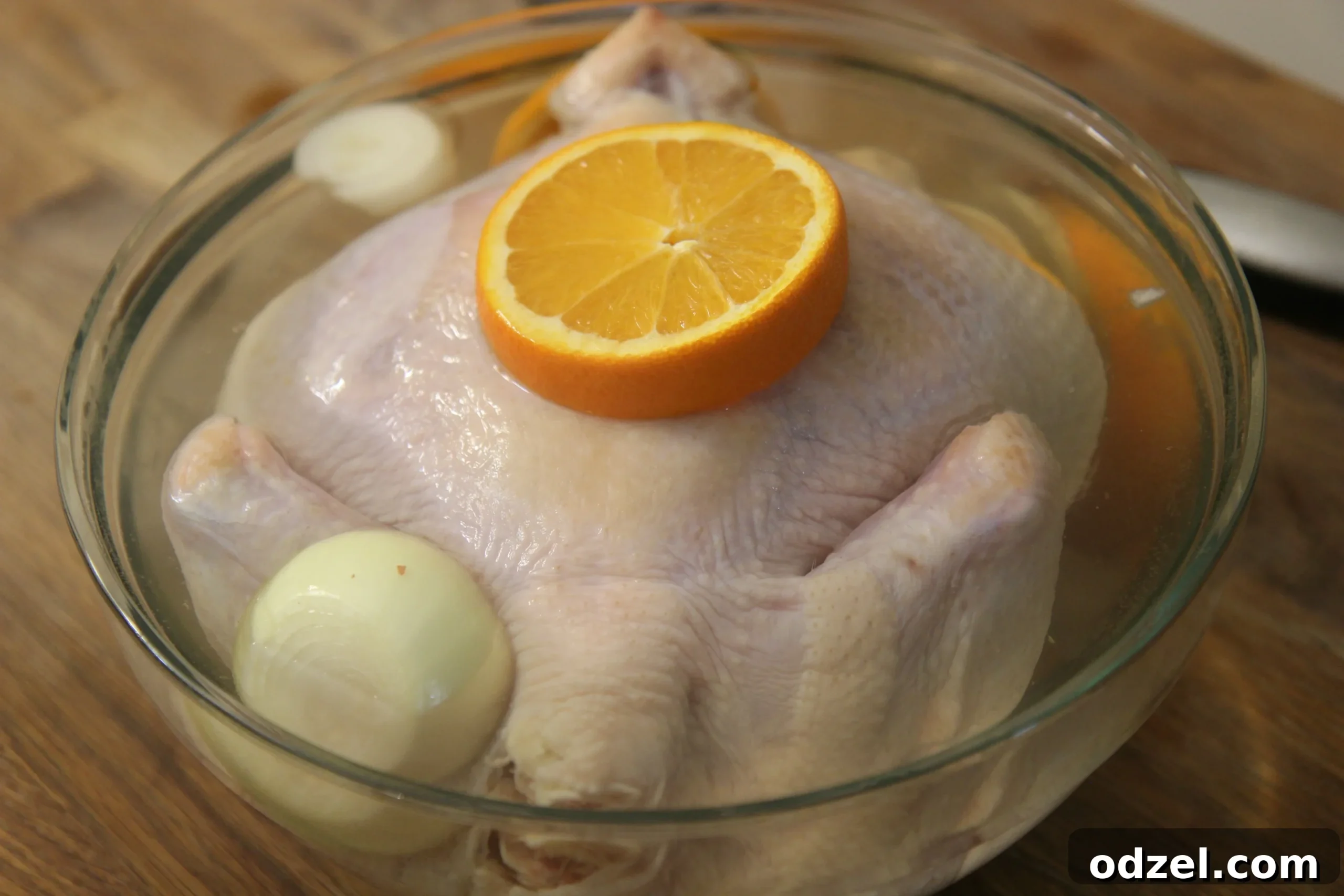 A whole chicken submerged in a flavorful brine mixture of water, salt, sugar, garlic cloves, sliced onions, and fresh orange wedges, ensuring deep flavor penetration and moisture retention.