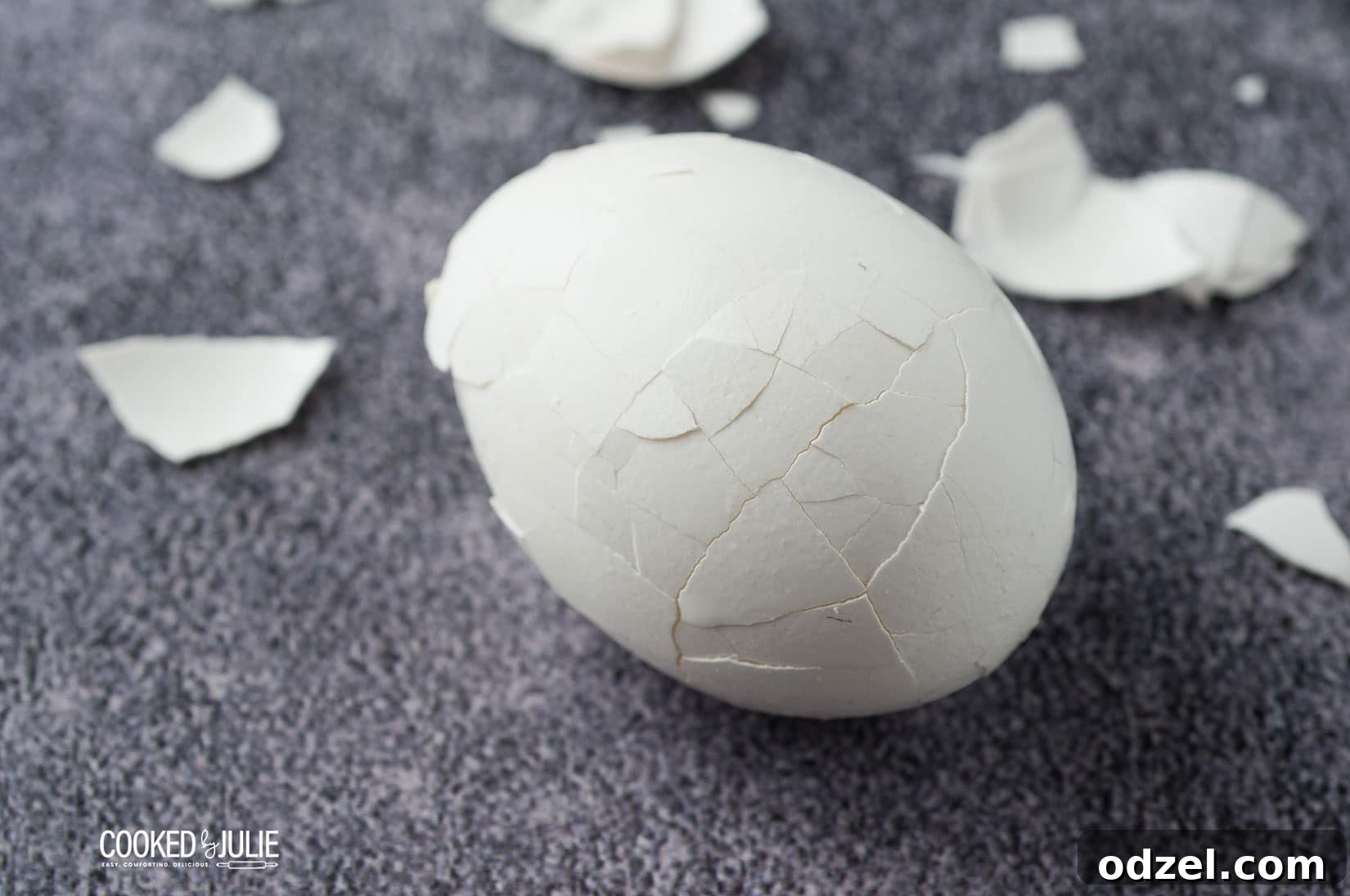 A white egg with the shell cracked and scattered egg shell pieces on a blue background, ready for peeling